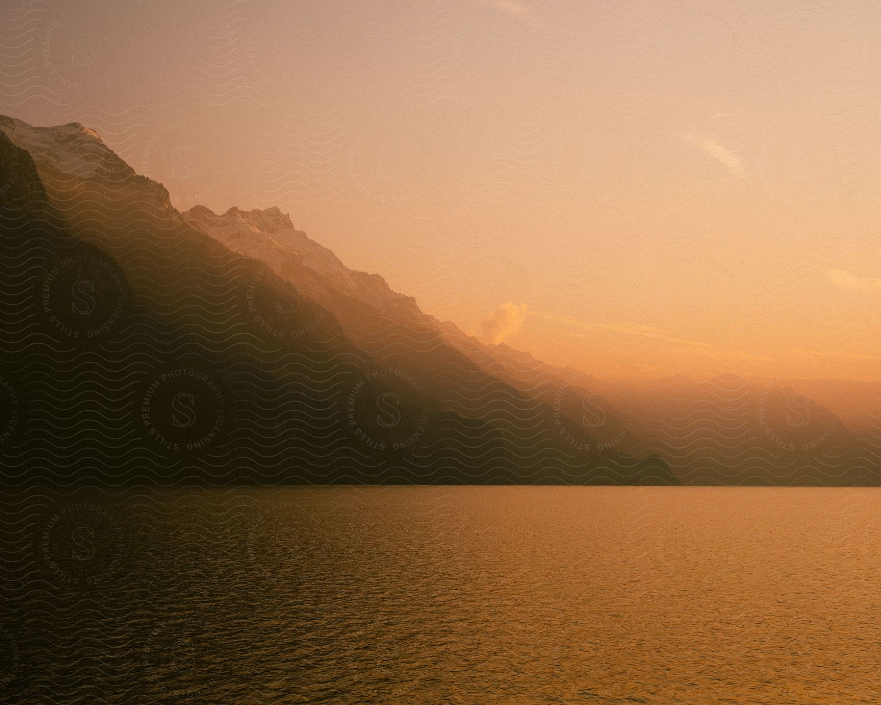 A mountain range sits next to a large lake at sunset.