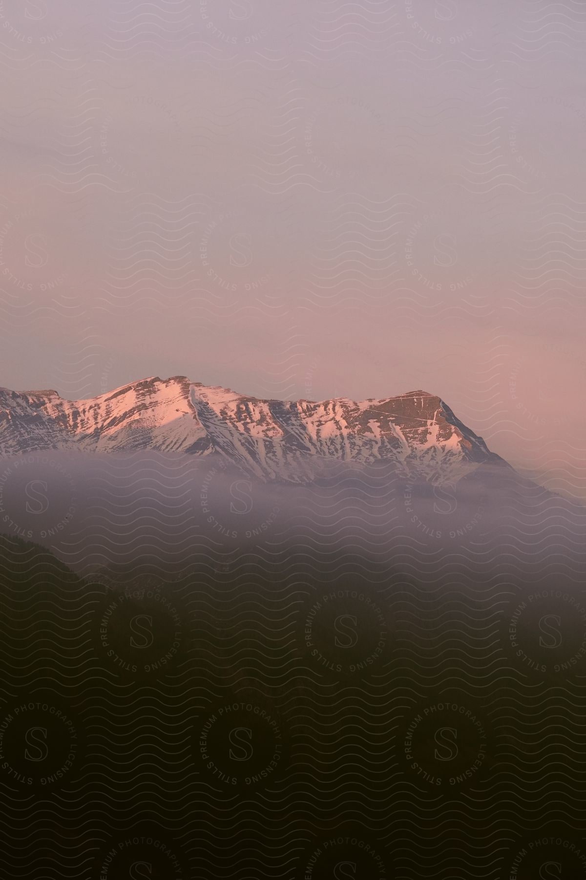 Sunlight shines upon snow covered mountains in the clouds and fog