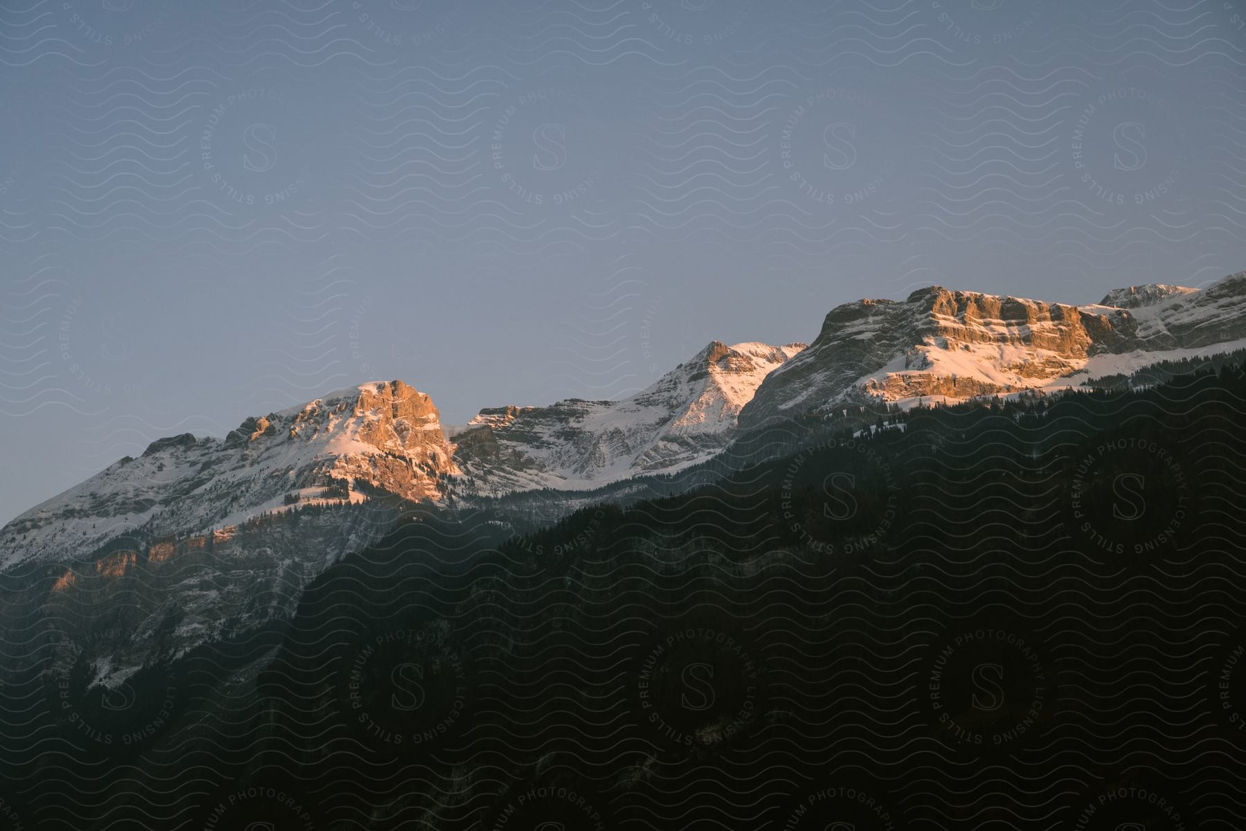 Sun shining on the snow dusted mountain ridge with forest trees covering the slope