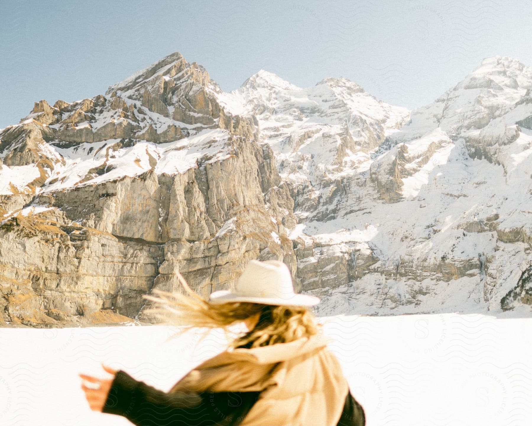 Woman with hair blowing in the wind, facing away, with snowy mountains in the background.