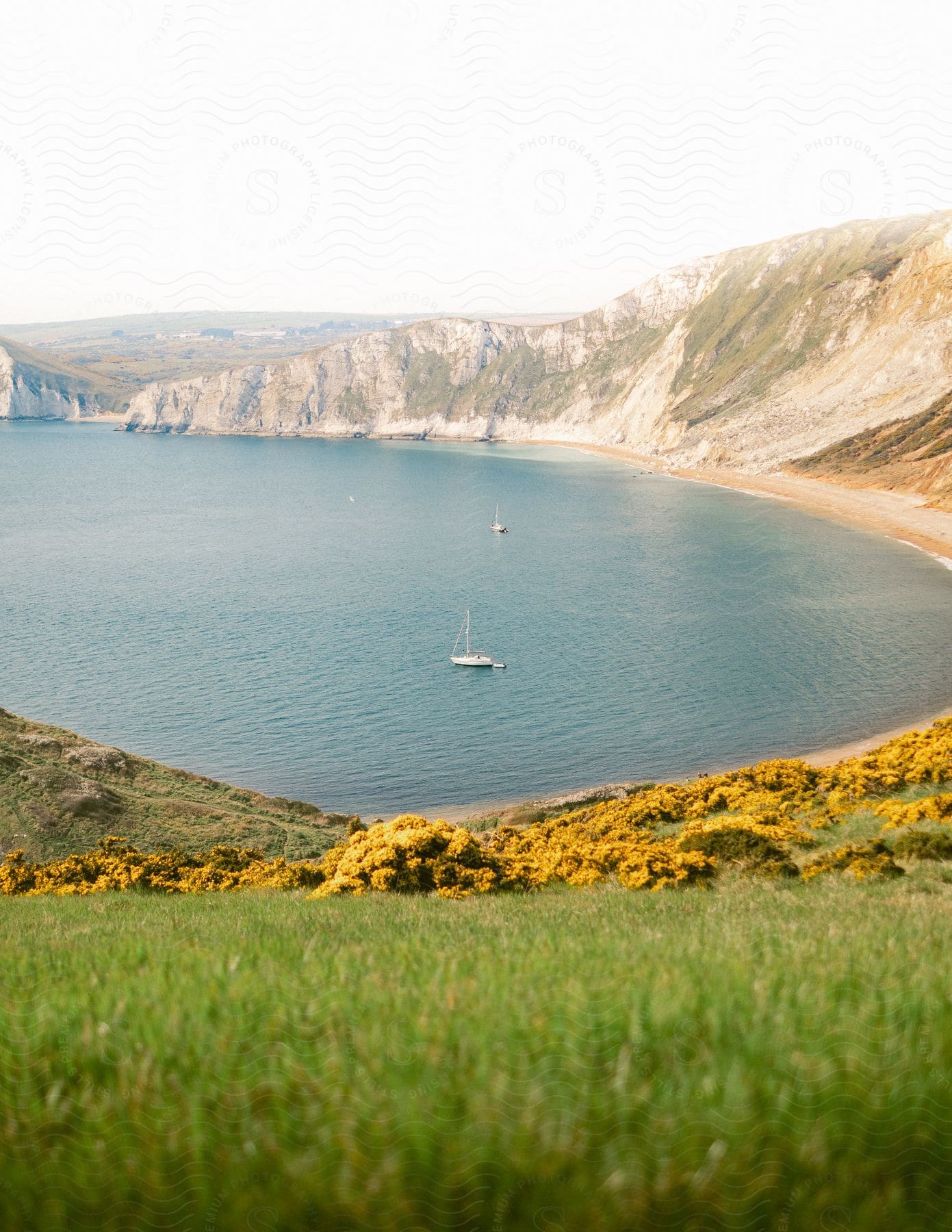 Bright green grass on the slope leading down to Worbarrow Bay where two sailboats are anchored near the beach
