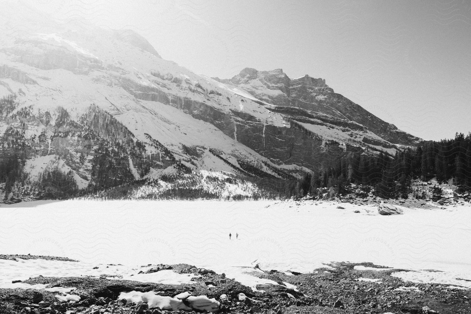 Two people standing at the snow covered base of a mountain on bright day