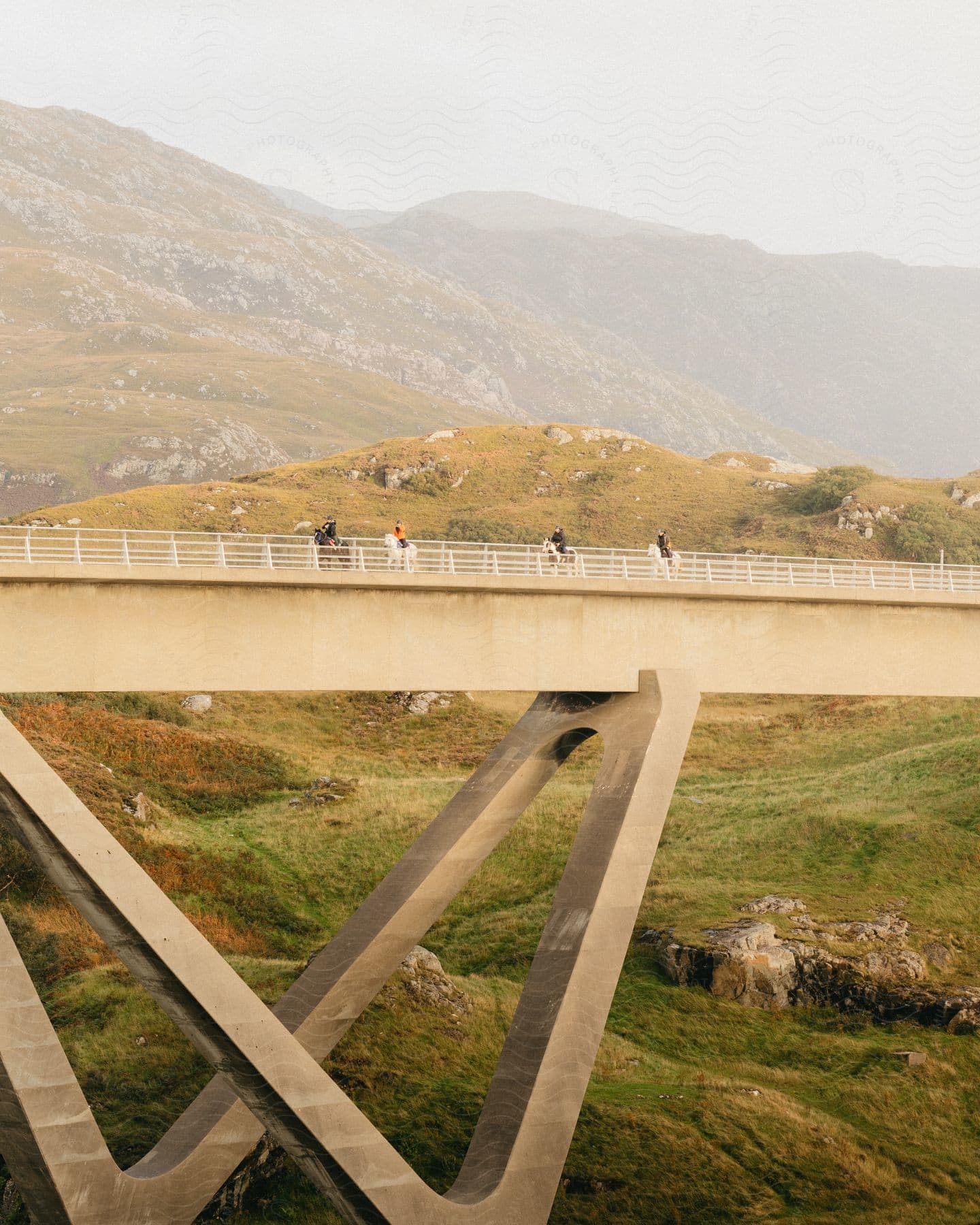 A group of people ride horseback across a concrete bridge in a mountainous area.