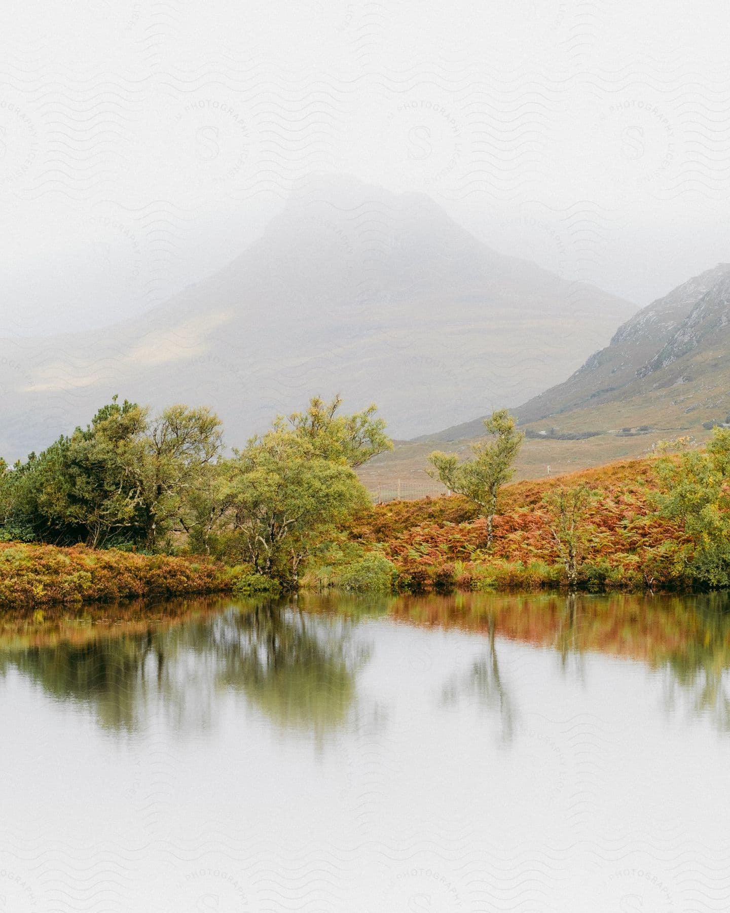 A serene landscape with a reflective lake surrounded by autumn foliage and a mysterious mountain in the background.