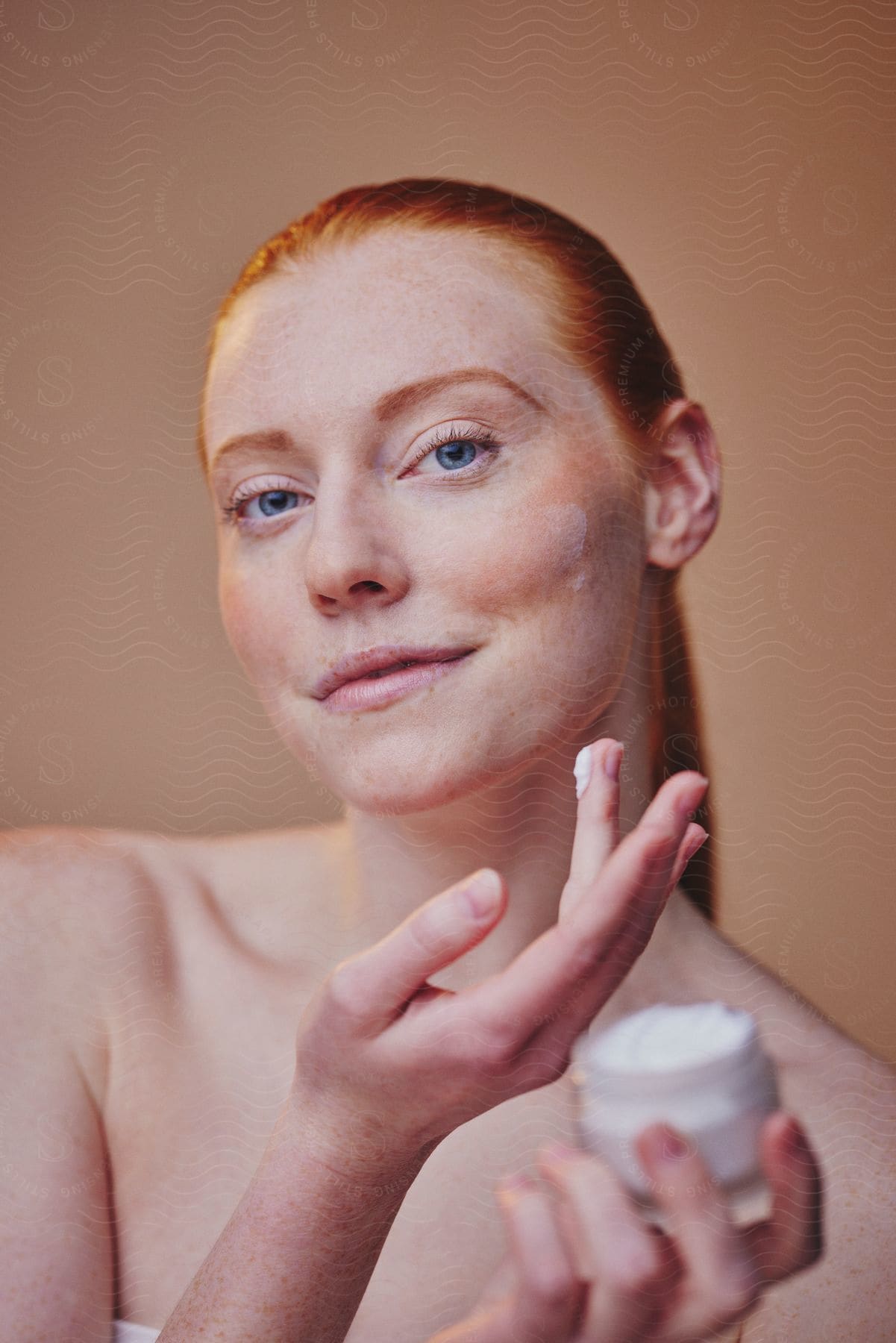 Smiling redheaded woman applies lotion to her face.