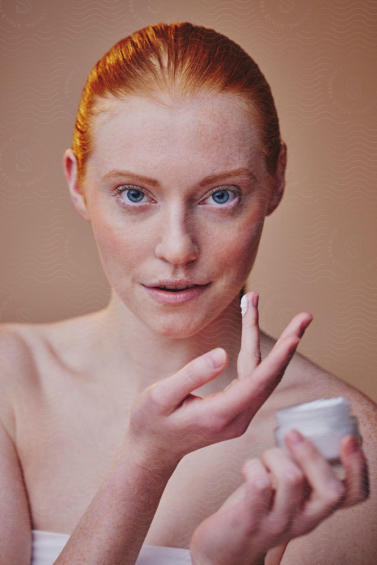 A red-haired woman holding a pot of face cream in her hands.