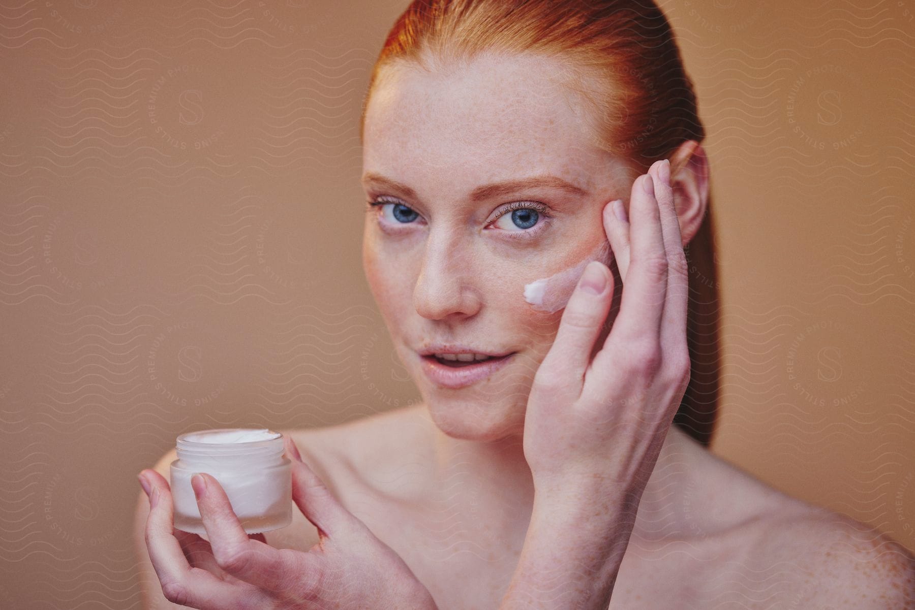 Close-up of redhead applying lotion to her cheek.