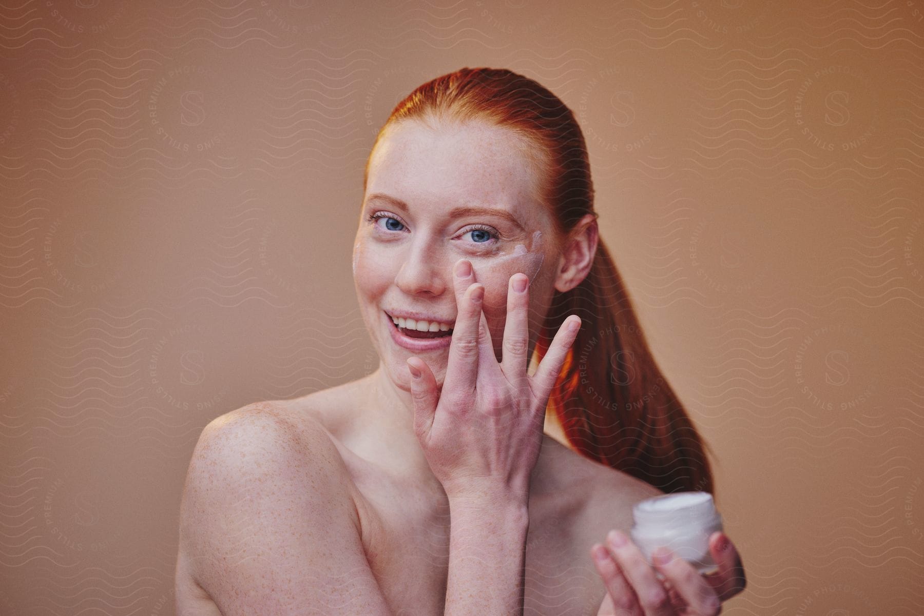 Red-haired Woman Applying Cream With Her Fingers Under Her Eyes And Holding A Small Pot In Her Other Hand