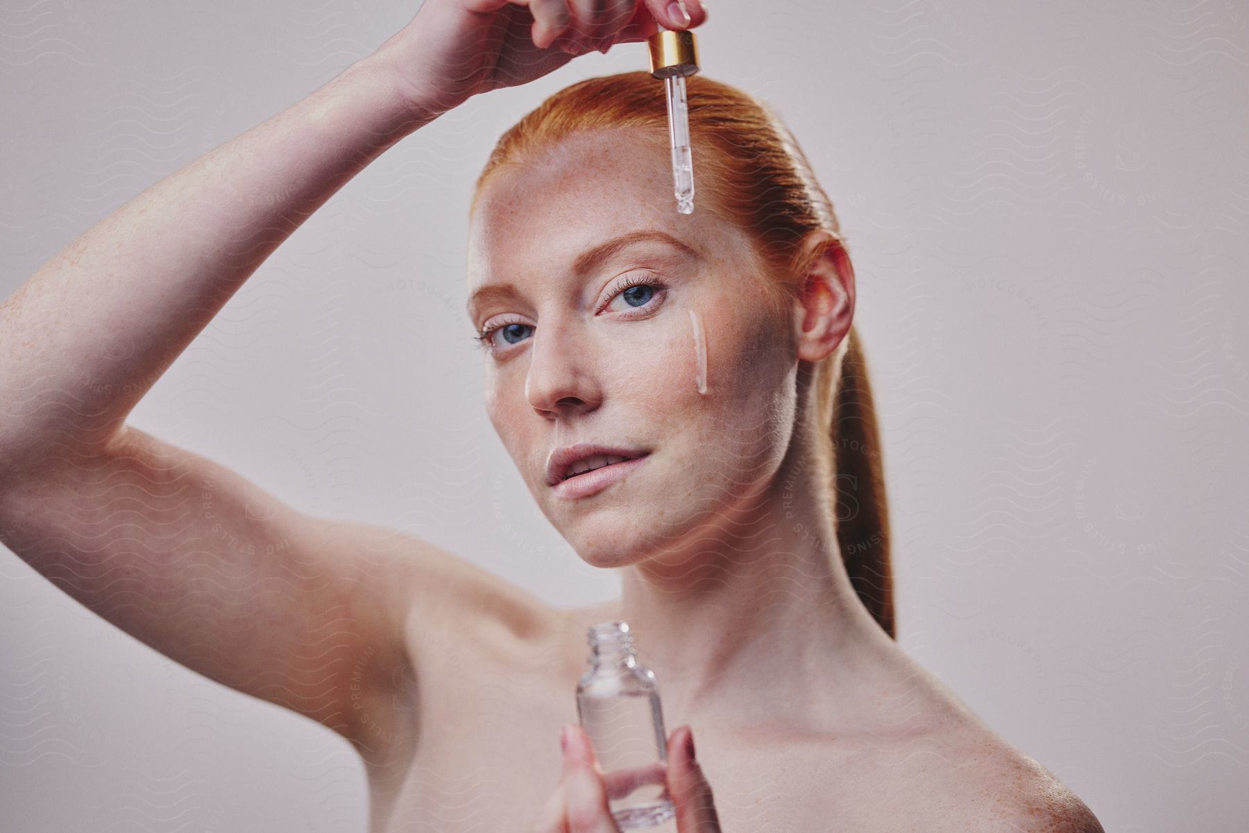 Red-haired Woman Dripping Serum On Her Face Against A Blurred White Background