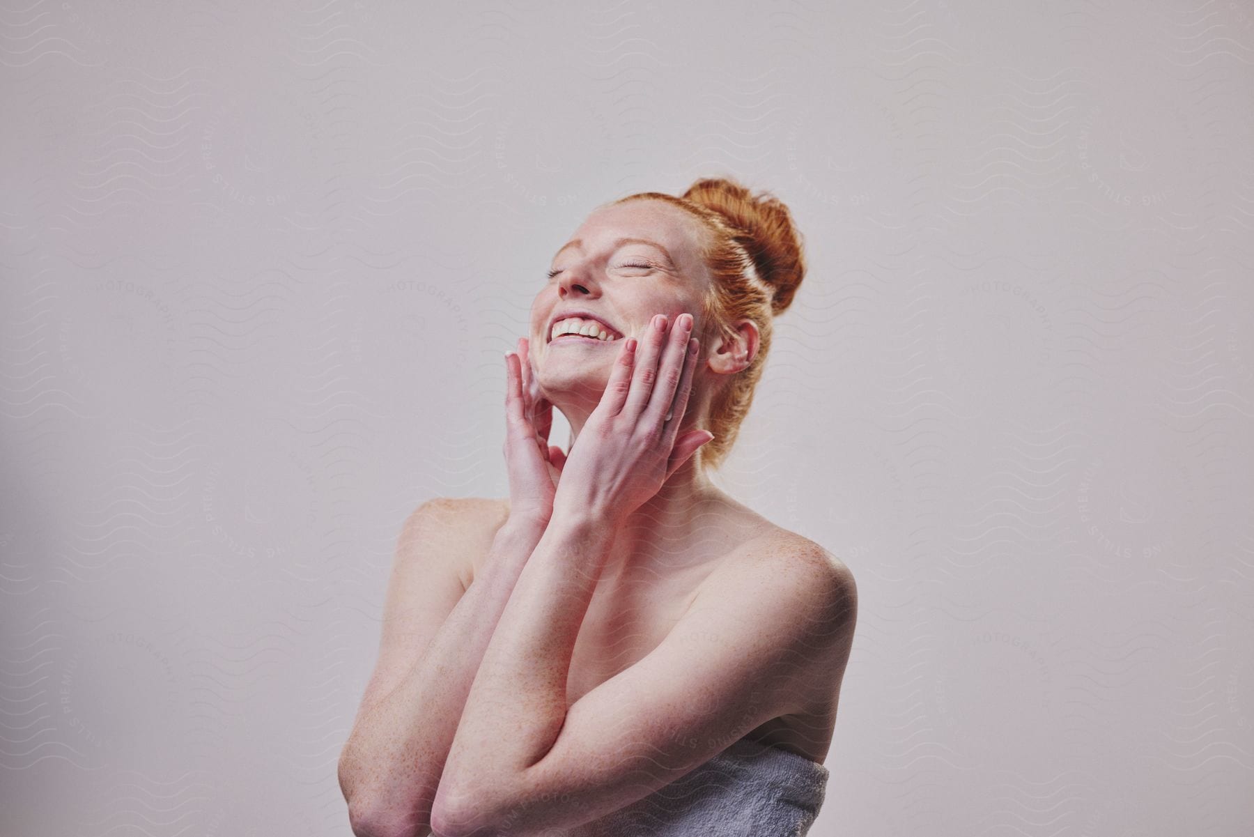 Young woman smiles with her eyes closed and tilts her head back as she washes her face with both hands