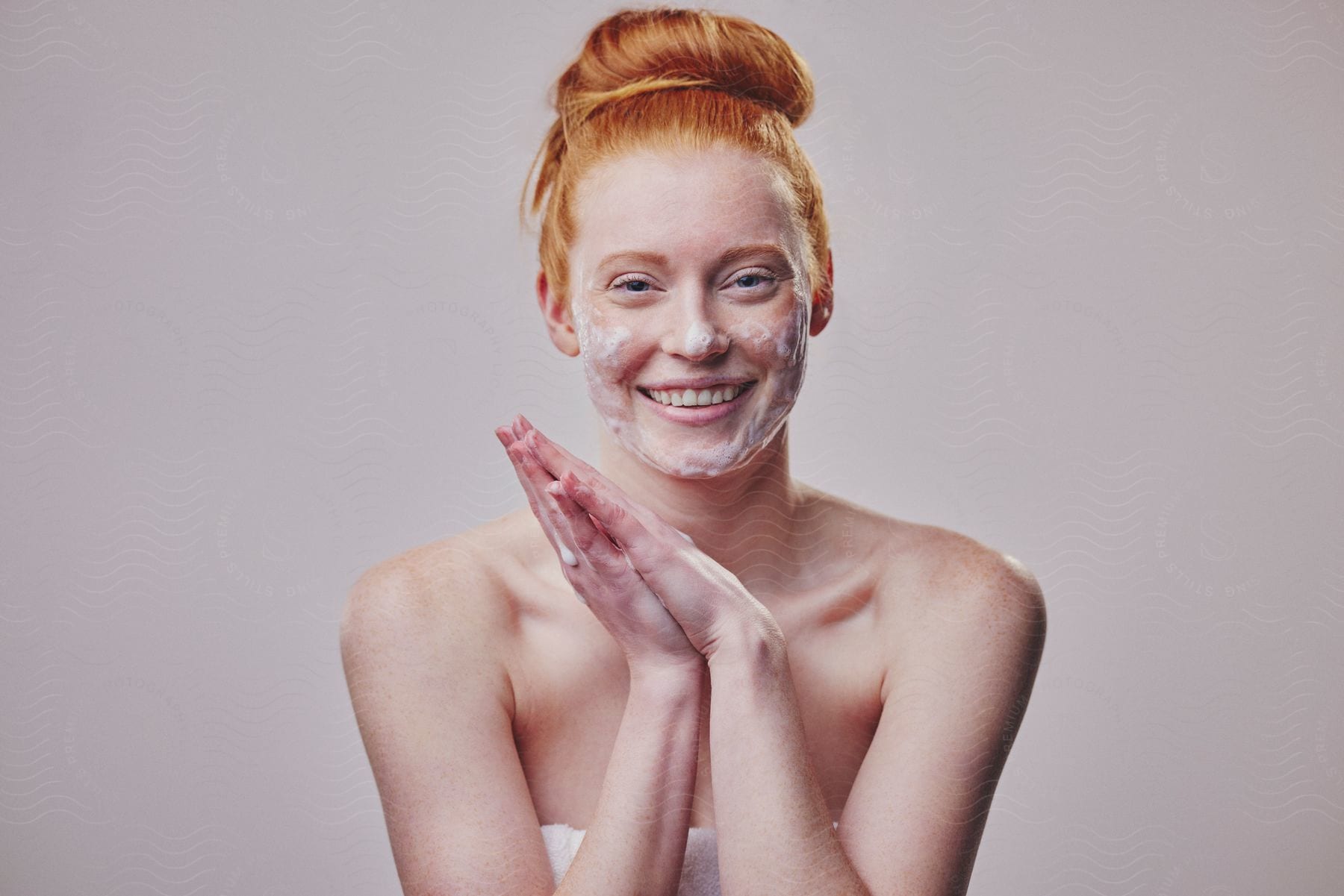 A woman rubs her hands together and smiles with soaps suds on her face.