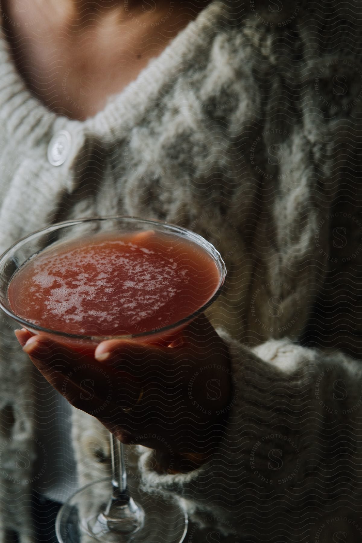 A person in a white knitted sweater holding a fizzy beverage