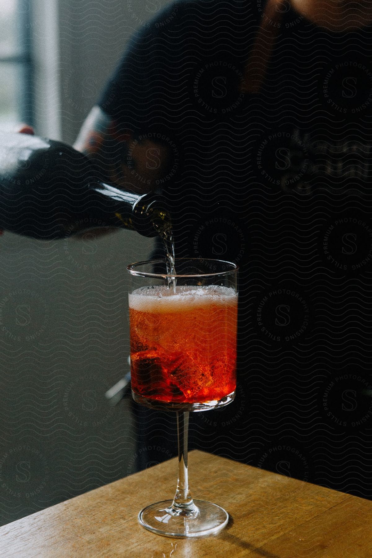 Person pours beverage into an ice filled glass from a dark bottle.