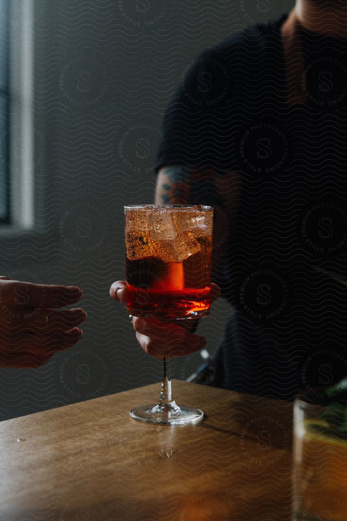 A person is handing someone else a beverage in a glass.