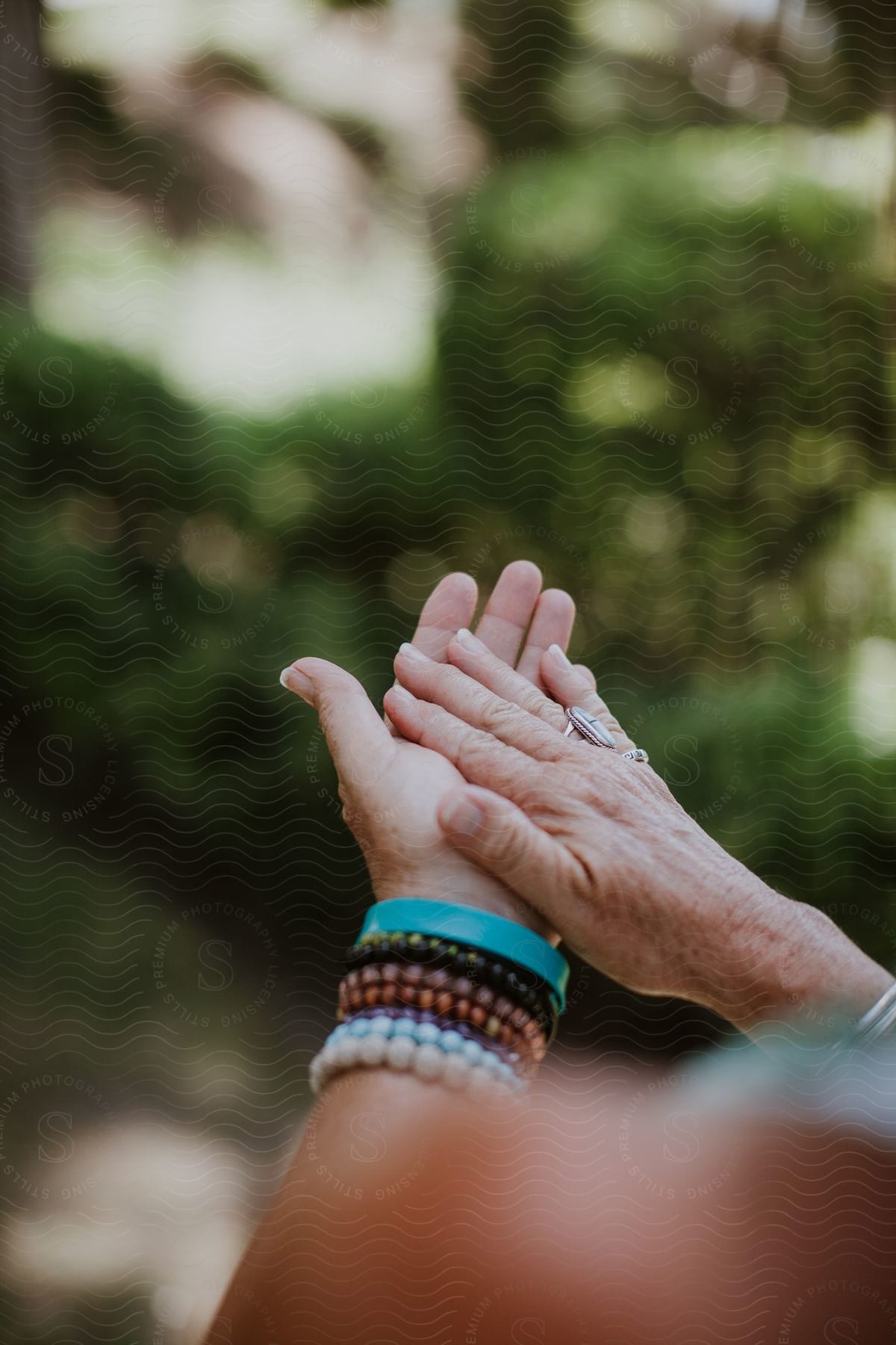 Palms together of a person with colorful bracelets and rings.