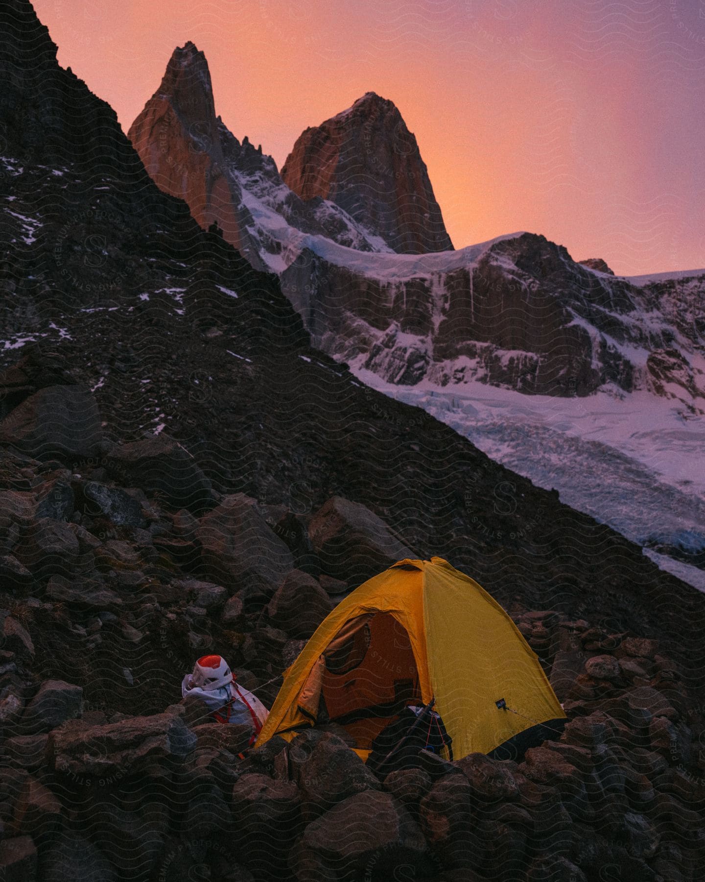 At the top of an icy mountain, a hiker has set up a yellow tent at sundown.