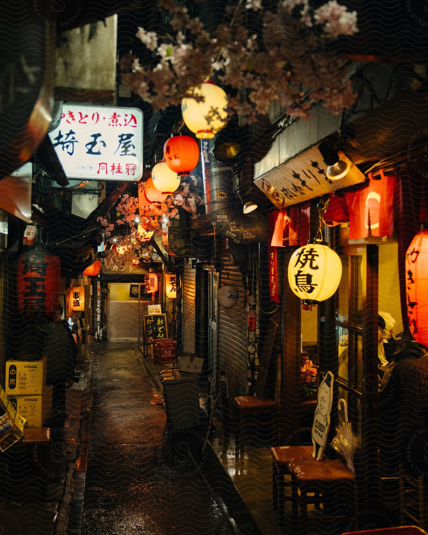 a narrow alleyway lined with small shops and restaurants, with red paper lanterns strung overhead casting a warm glow