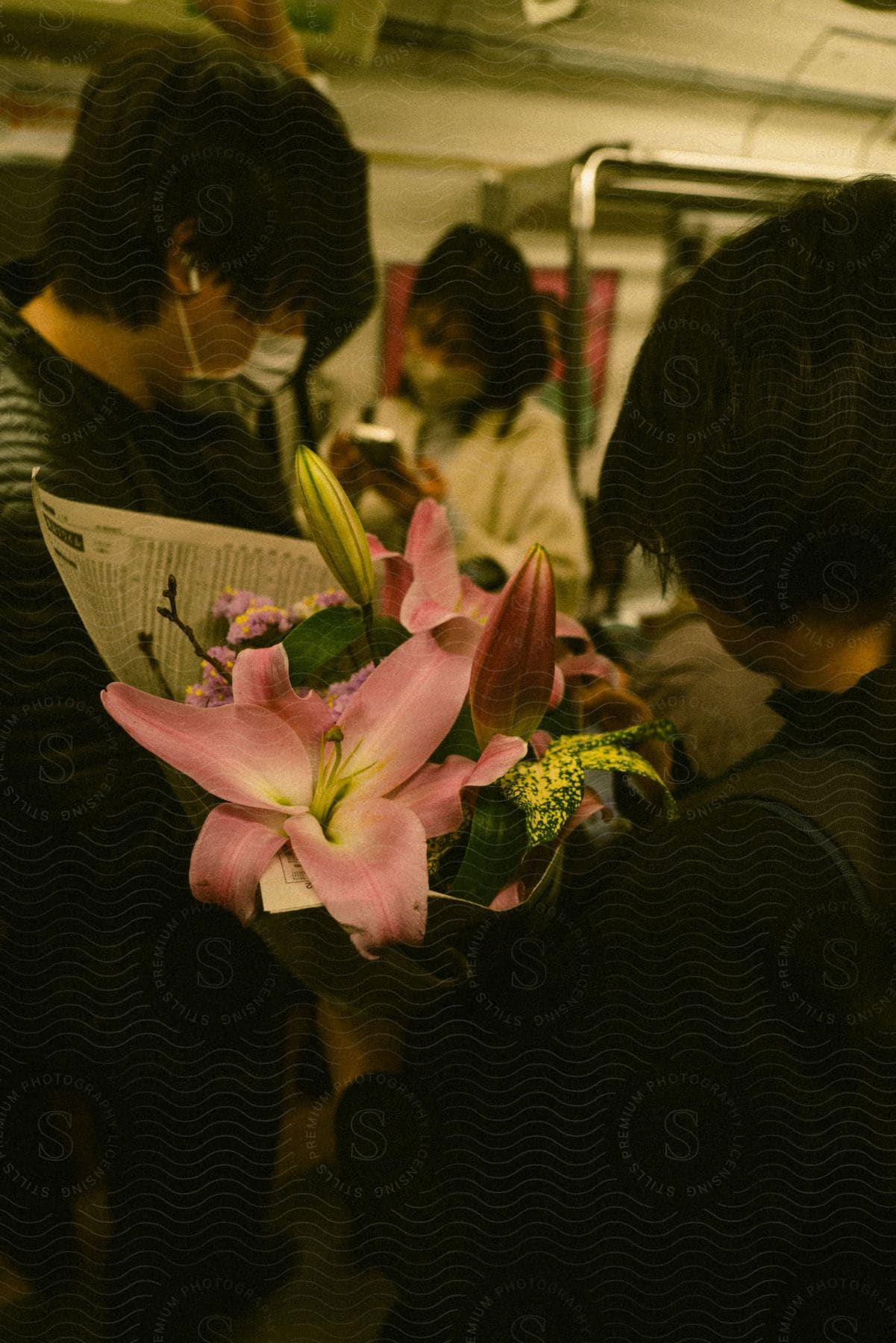 Woman holding a bouquet of lily flowers, inside a public transport carriage and around are other passengers.