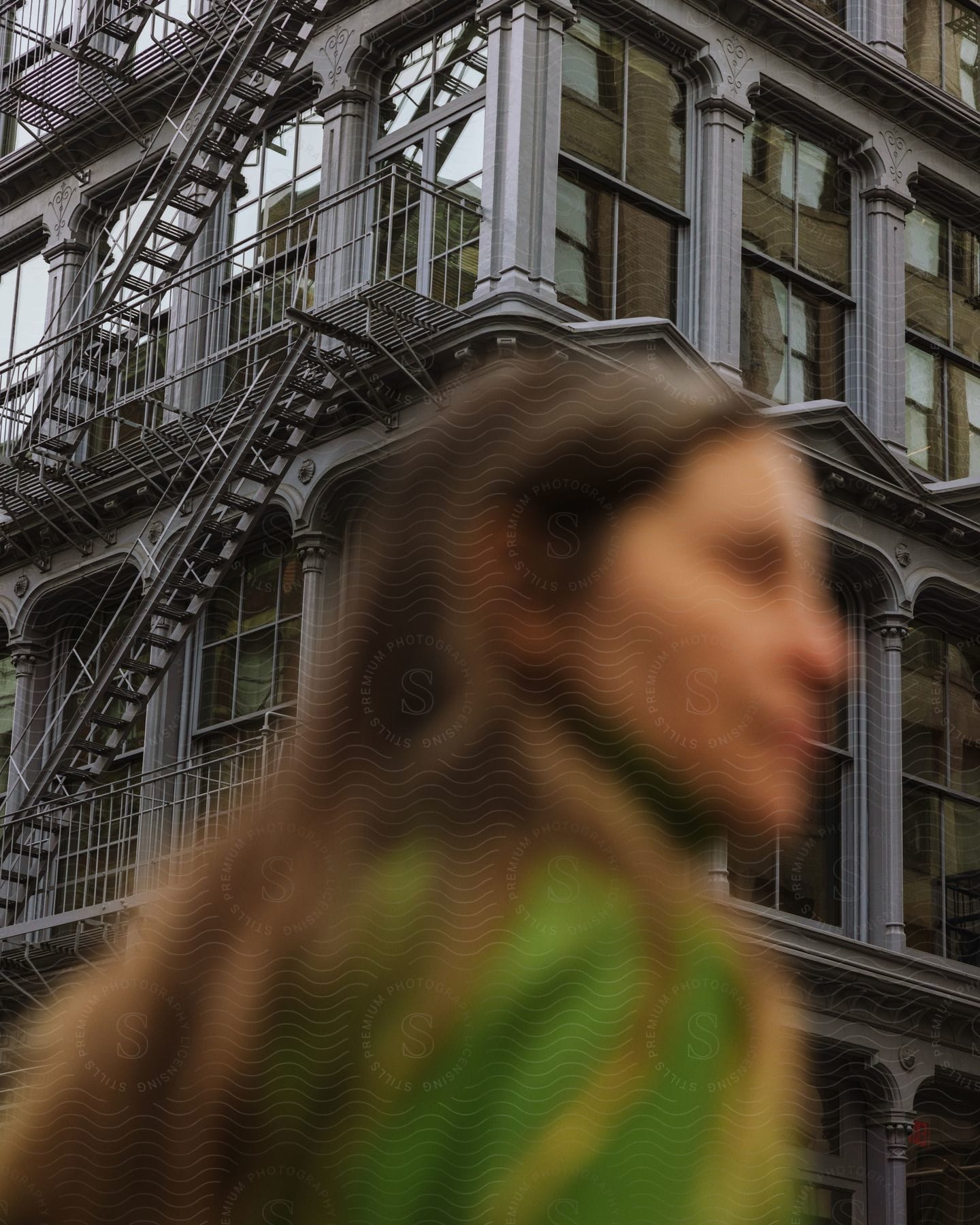 Blurry face of a woman standing in front of a grey, multi-story apartment building.