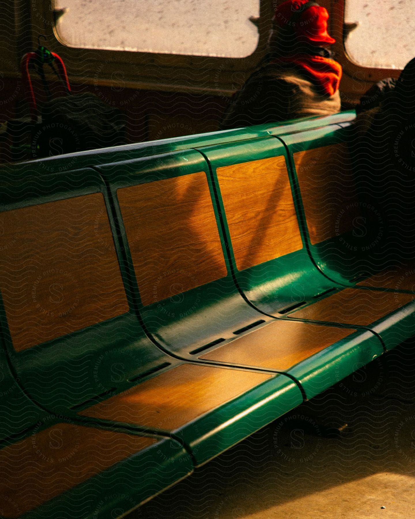 A red-hatted passenger sits on a green, wooden ferry bench next to a window, with a roller bag with a red handle nearby