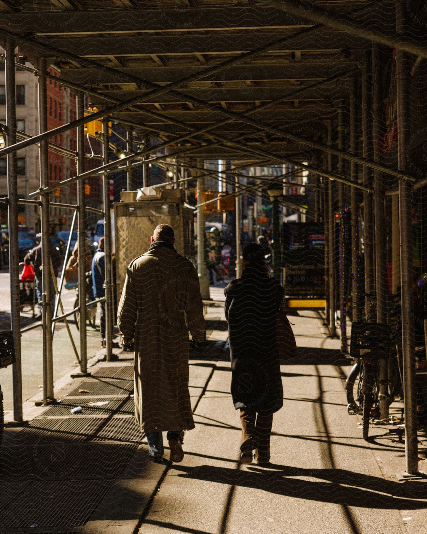 Two people walking through scafolding across a side walk in the city
