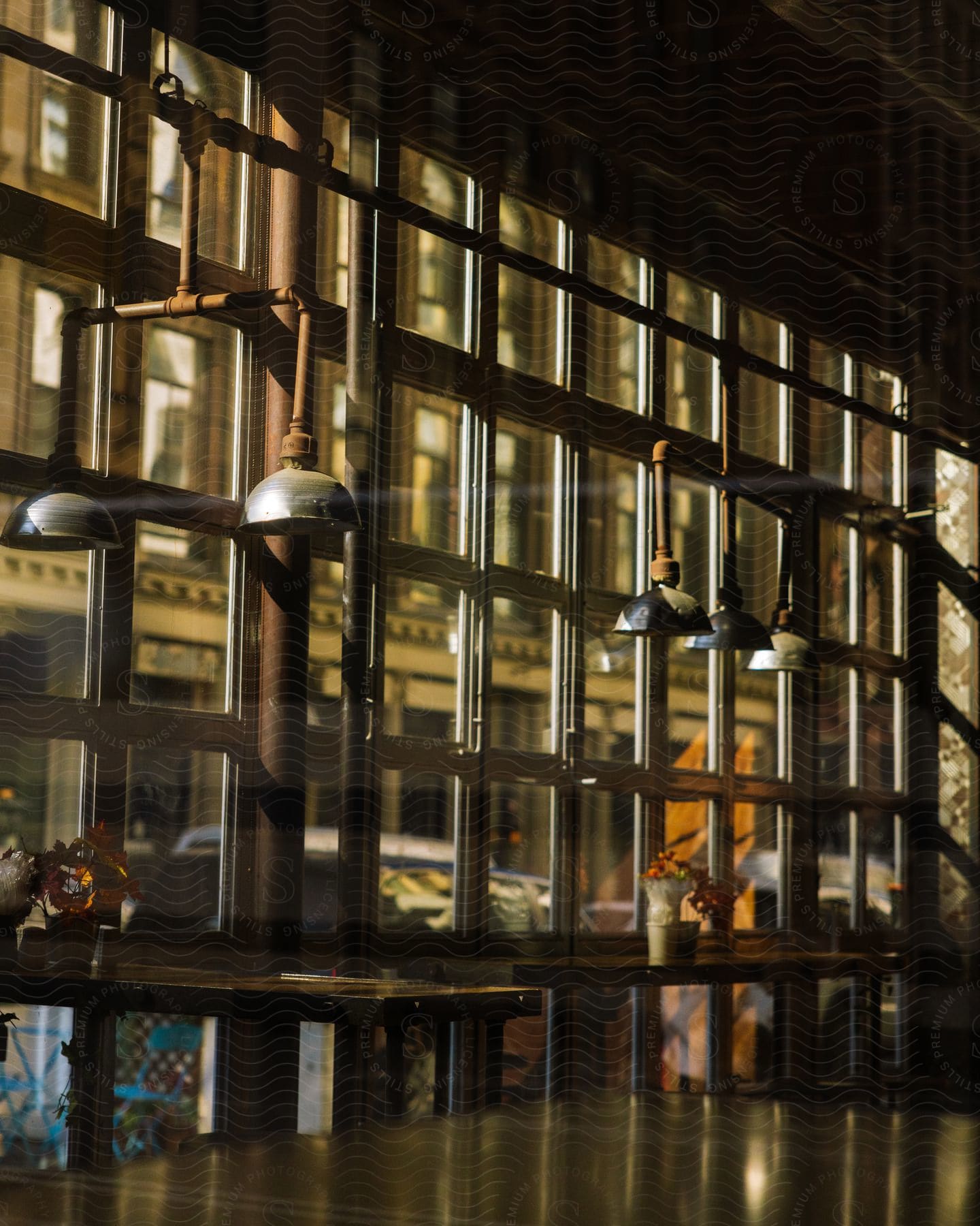 Gazing through the window, an empty coffee shop bathed in soft morning light with a row of dark, unlit bulbs hanging from the ceiling.