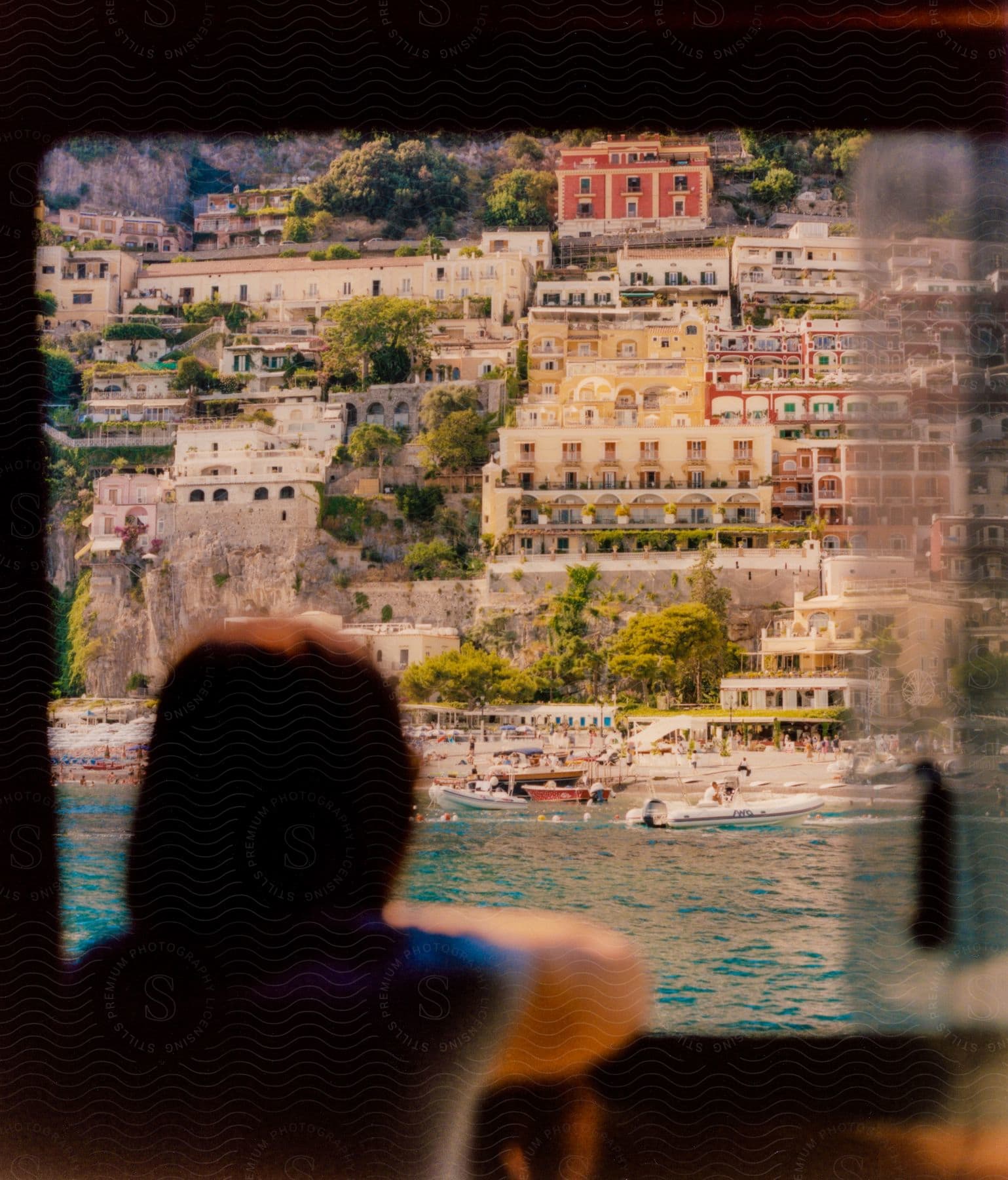 A woman sits in a boat, looking out through the window onto the river as other boats pass by, with a city view on the opposite side of the river.