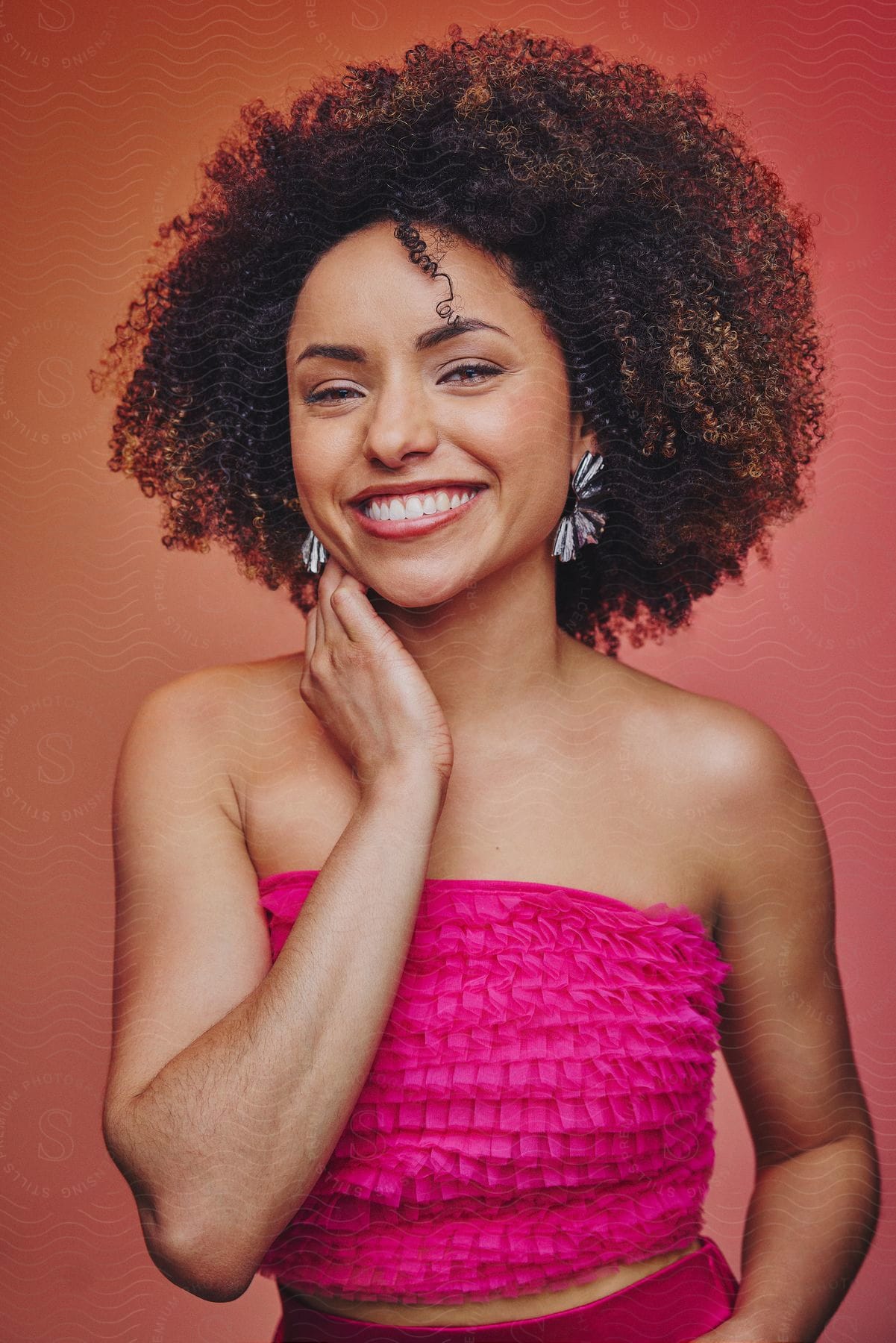 A woman with a smiling face poses against a red background, wearing a pink top.