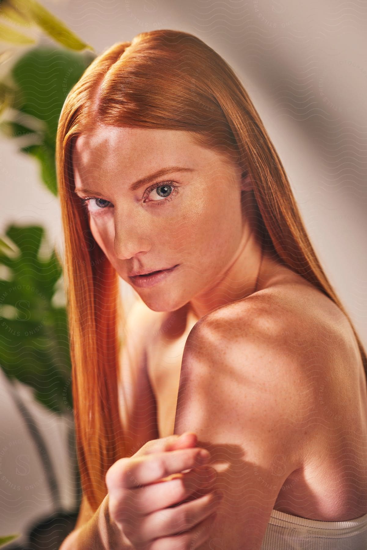 Young woman with long red hair and bare shoulders turns her head to look into the camera