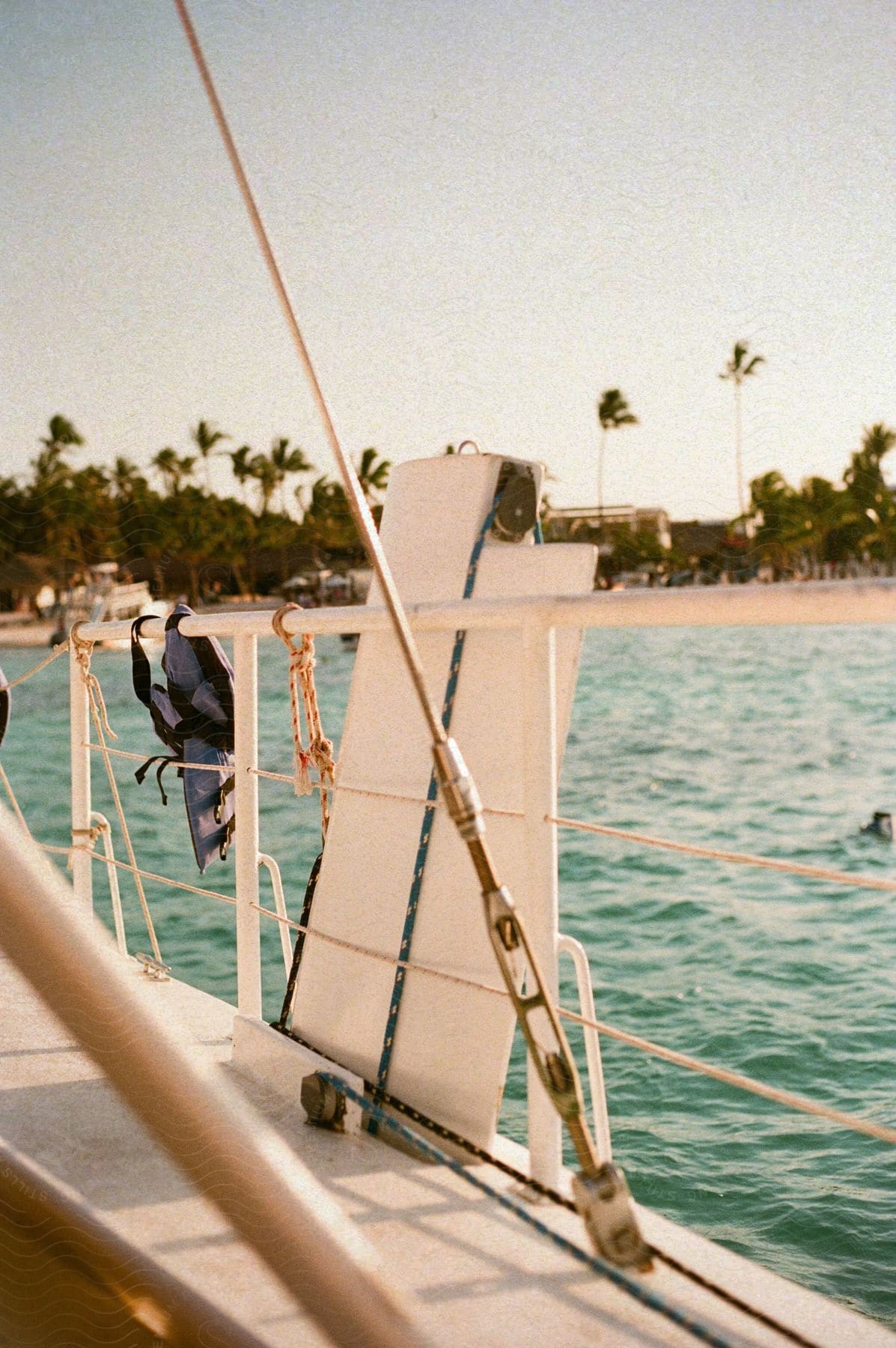 Deck of a boat sailing off the coast of a beach with palm trees