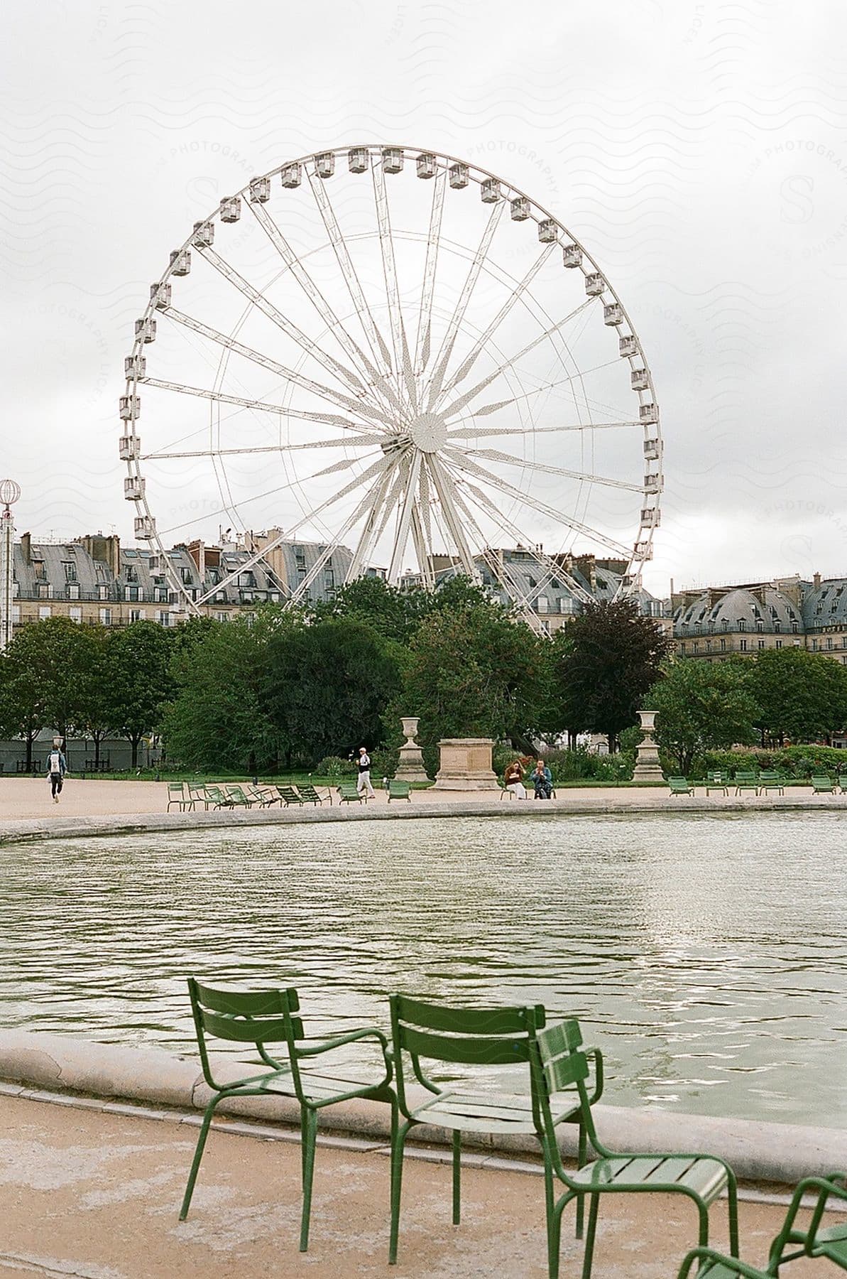 People walking and sitting at the pond under the ferris wheel at the Jardin des tuileries in Paris