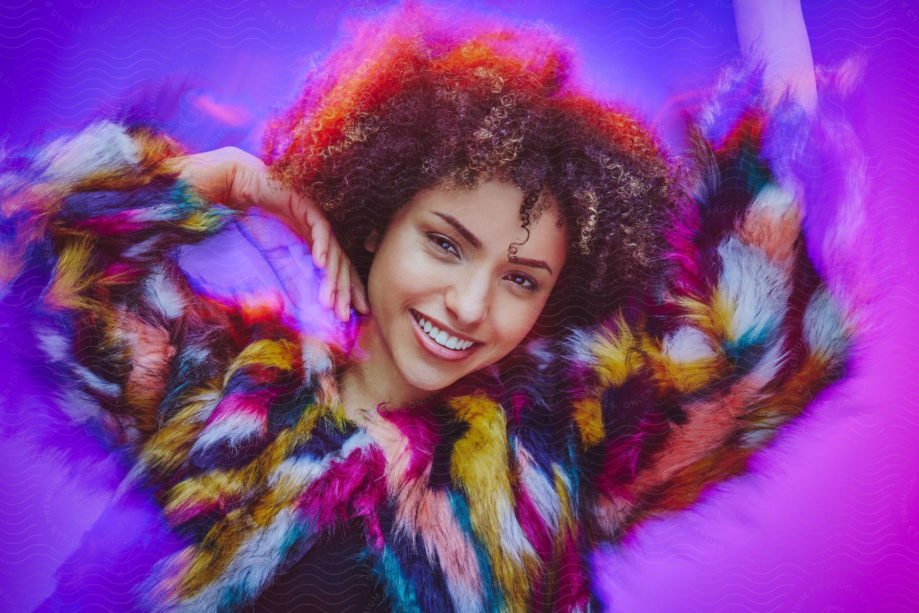 Young woman wearing a colorful fur jacket is dancing with her arms in the air