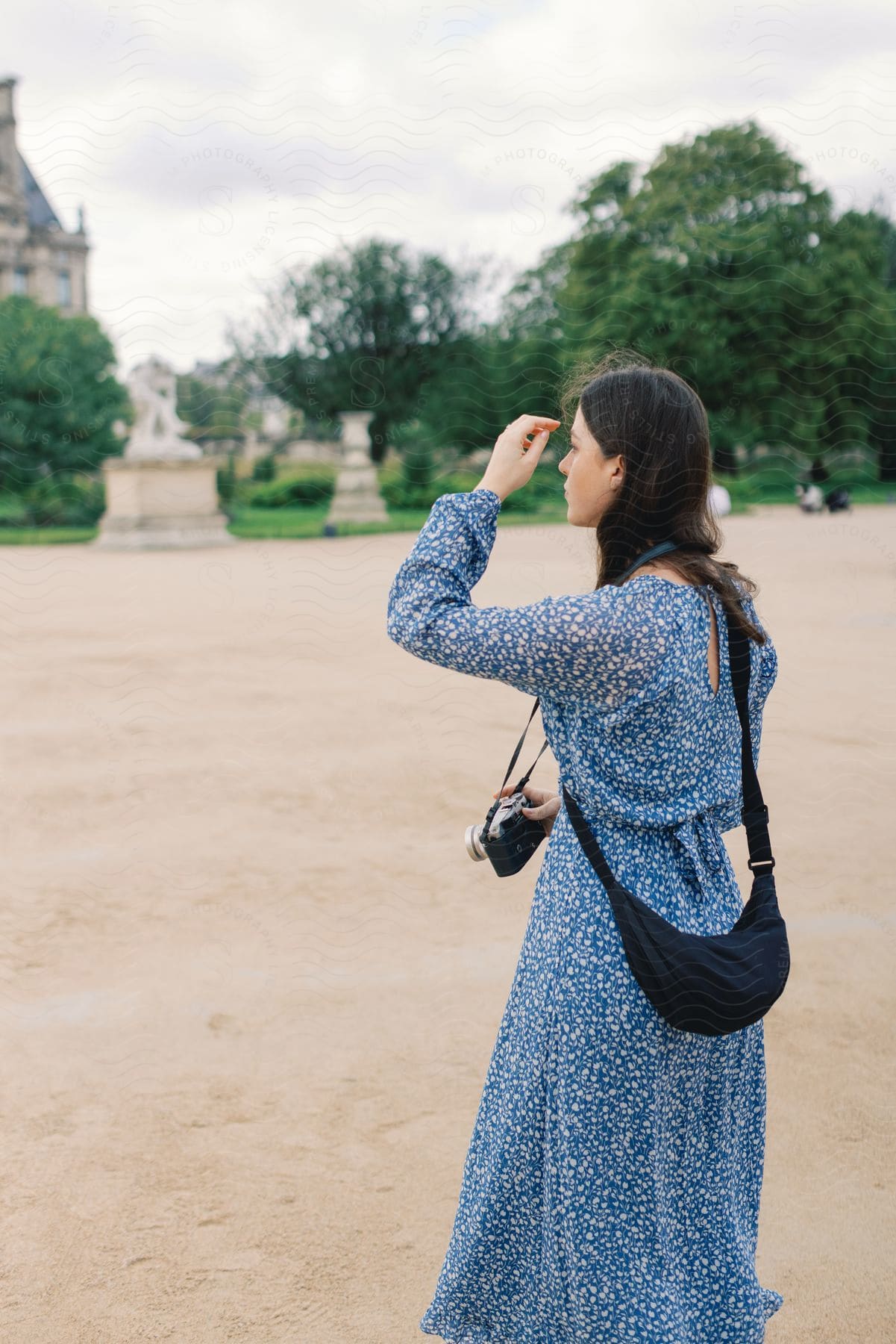 Woman in a blue floral dress with a camera looking into the distance in a park.