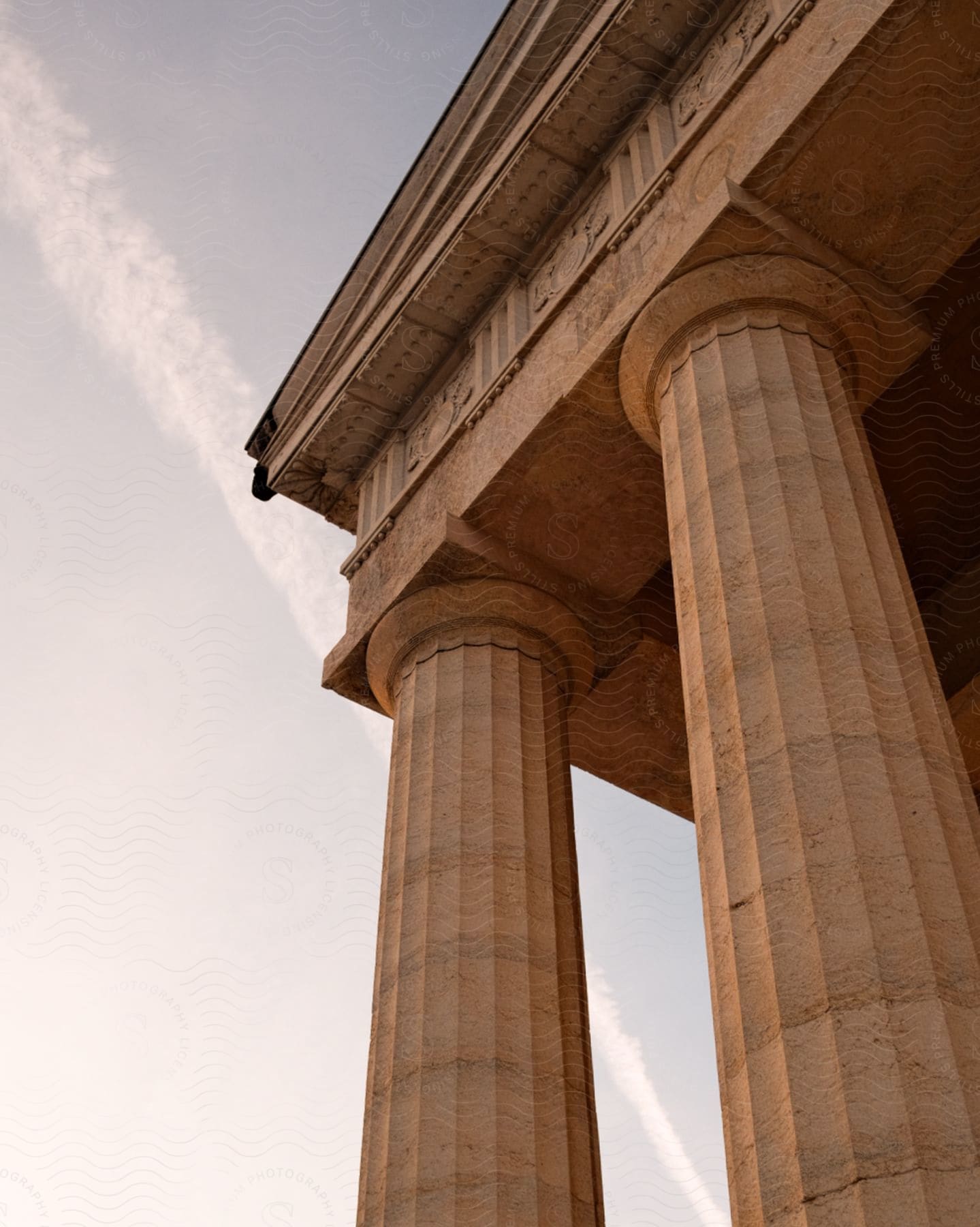 Low angle view of neoclassical columns against a clear sky with contrail.