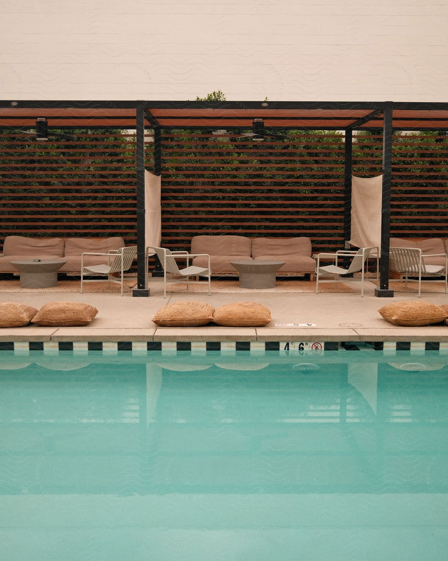a swimming pool with a pergola casting shade over a lounge area on the patio behind it.