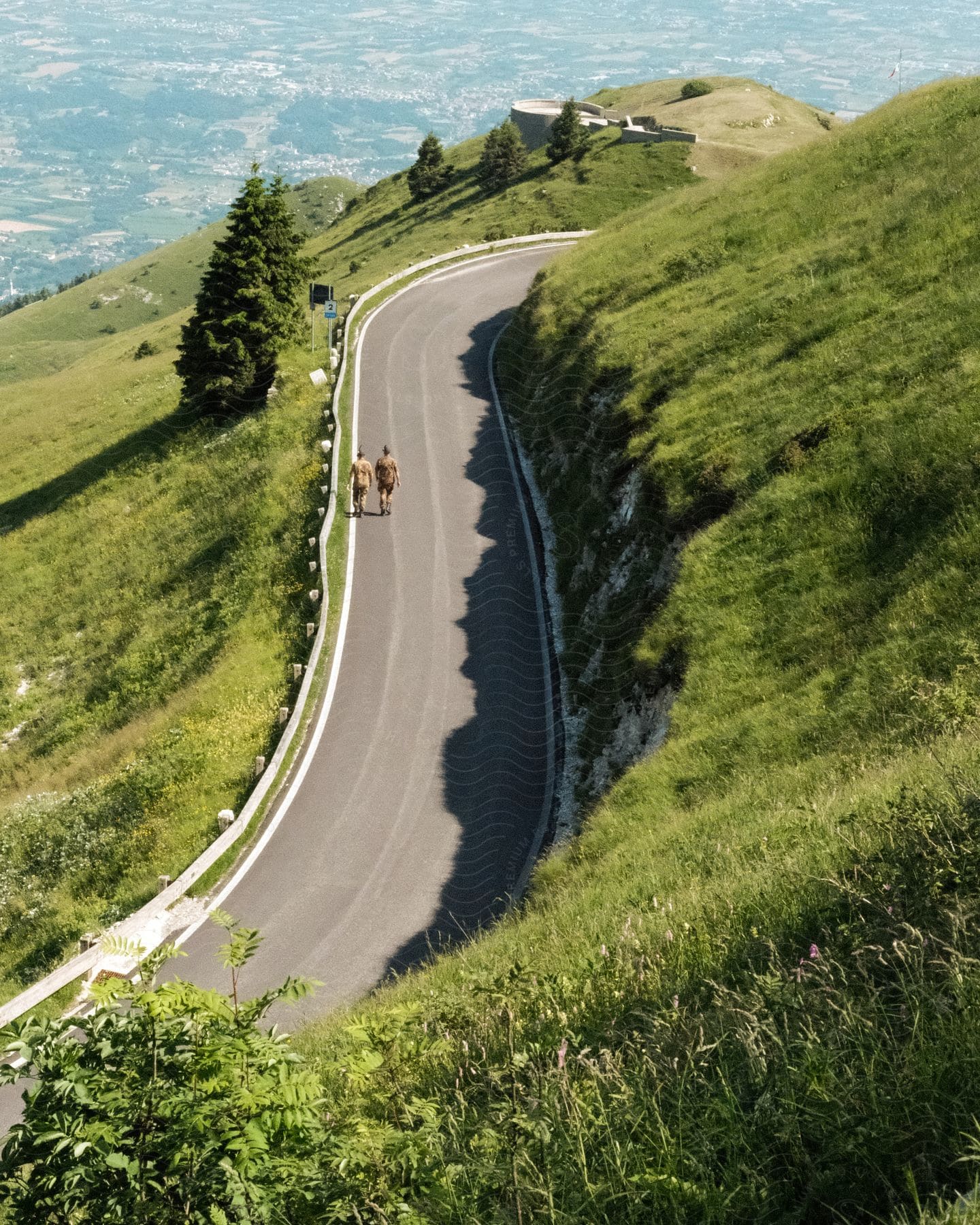 Aerial view of two men walking up a winding road on a green mountain