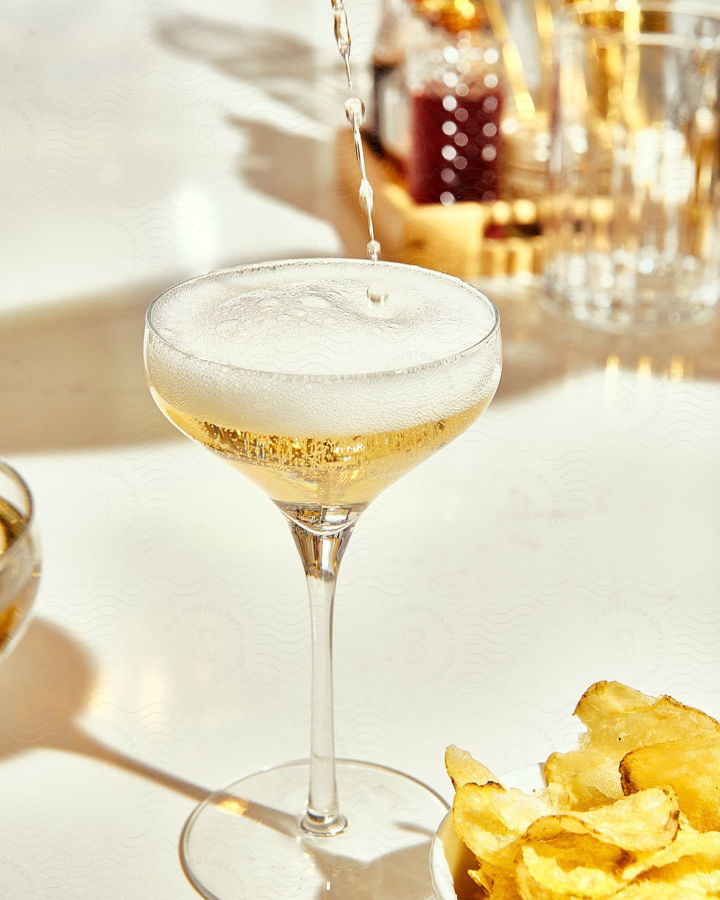 Wine poured into a glass on a table next to a bowl of potato chips.