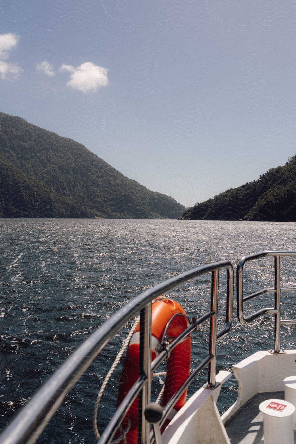 Green mountains on horizon, body of water below as seen from boat railing during the day