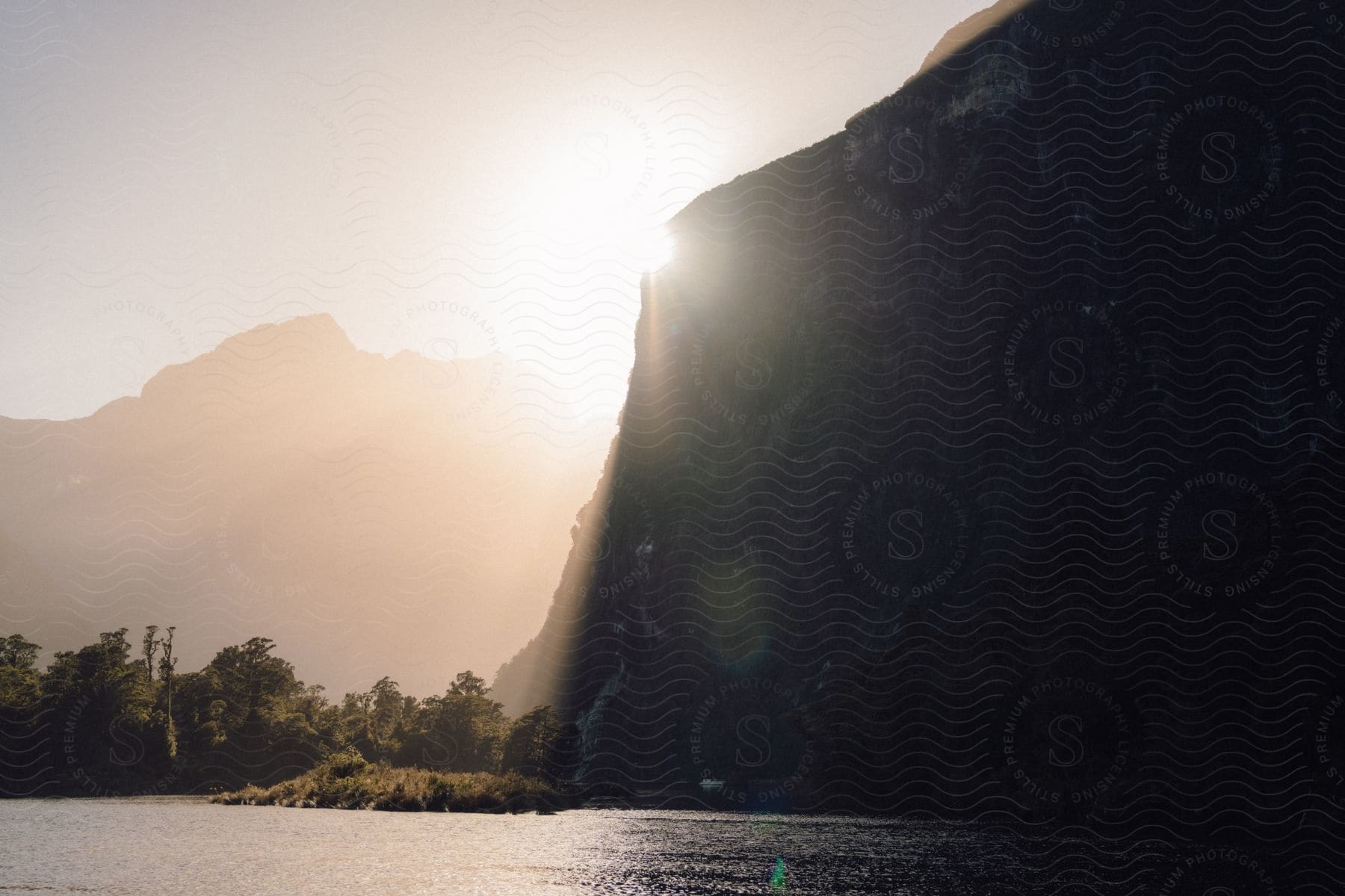 Sun shining brightly over a mountain cliff along the coast in a hazy sky with mountains in the distance