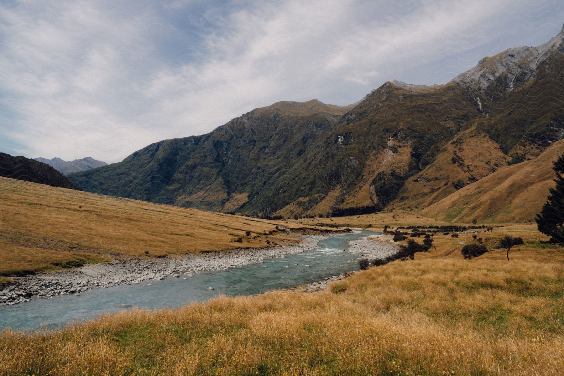 A creek flows through a meadow at the base of a mountain range on a cloudy day.