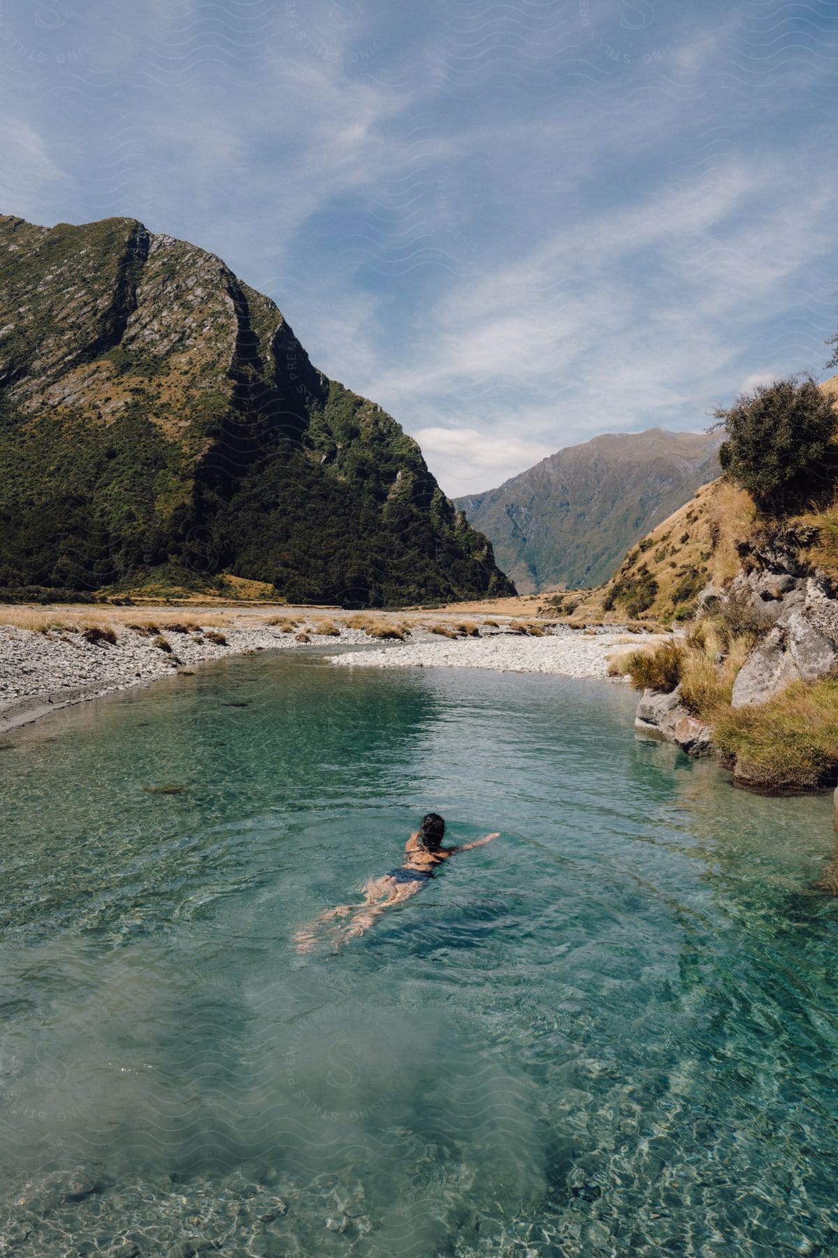 A person swimming in a small lake with crystal clear water in a region with some mountains