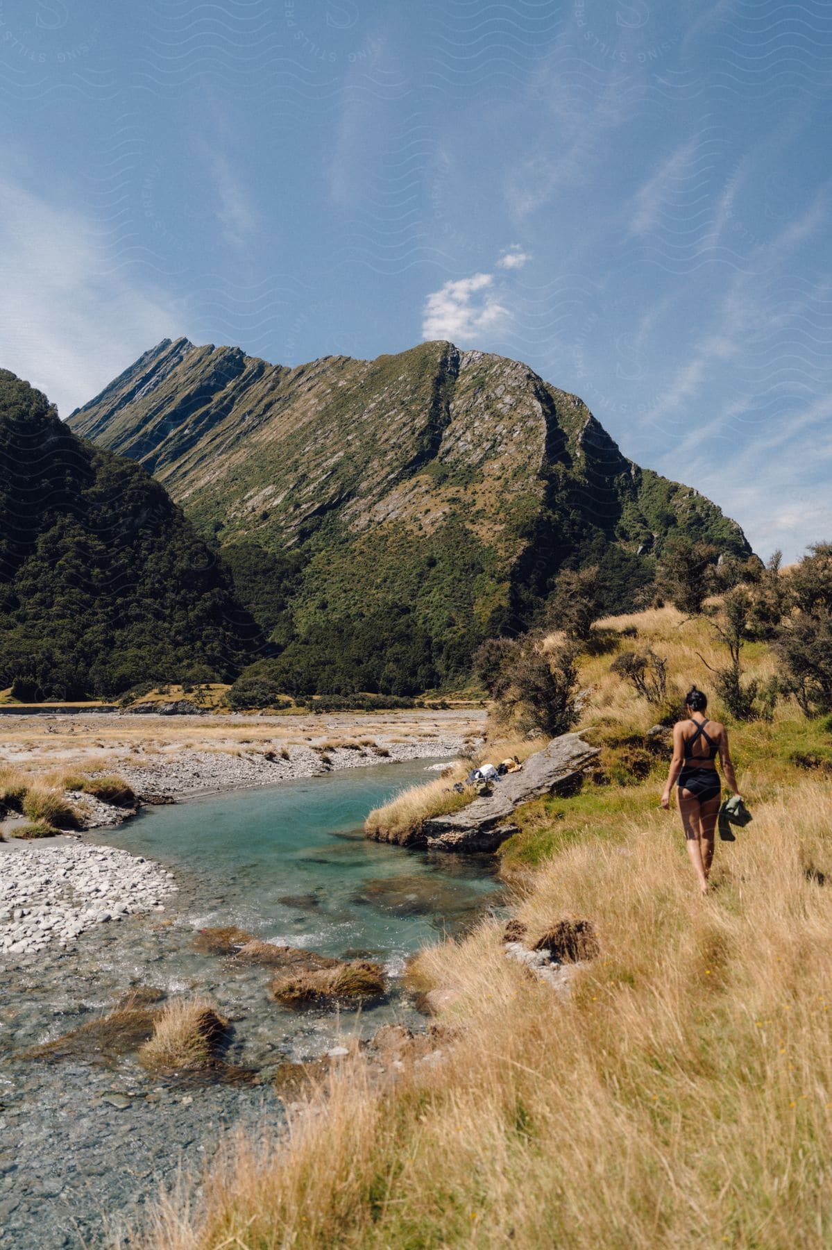 A woman in a swimsuit walks on a grassy area next to a stream