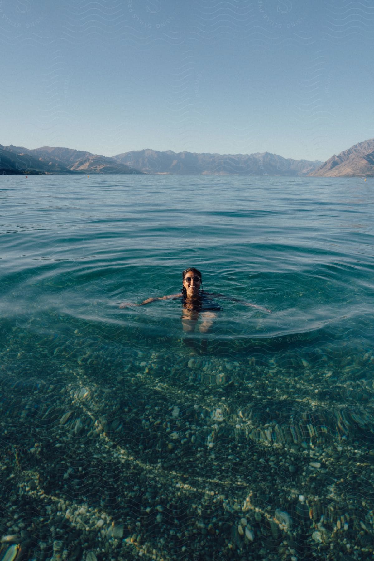 A person swims in crystal blue water with mountains in the background.