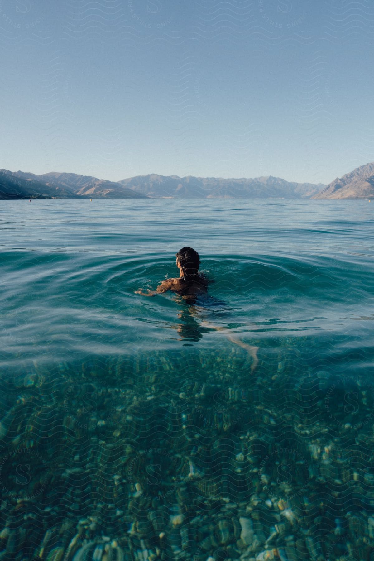 Woman swimming in clear water with mountains in the distance