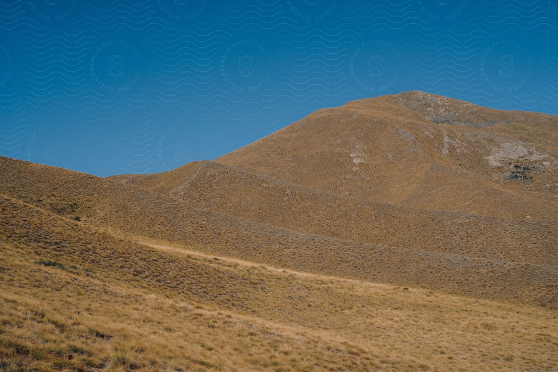 A large hill of land with low vegetation in contrast to blue sky