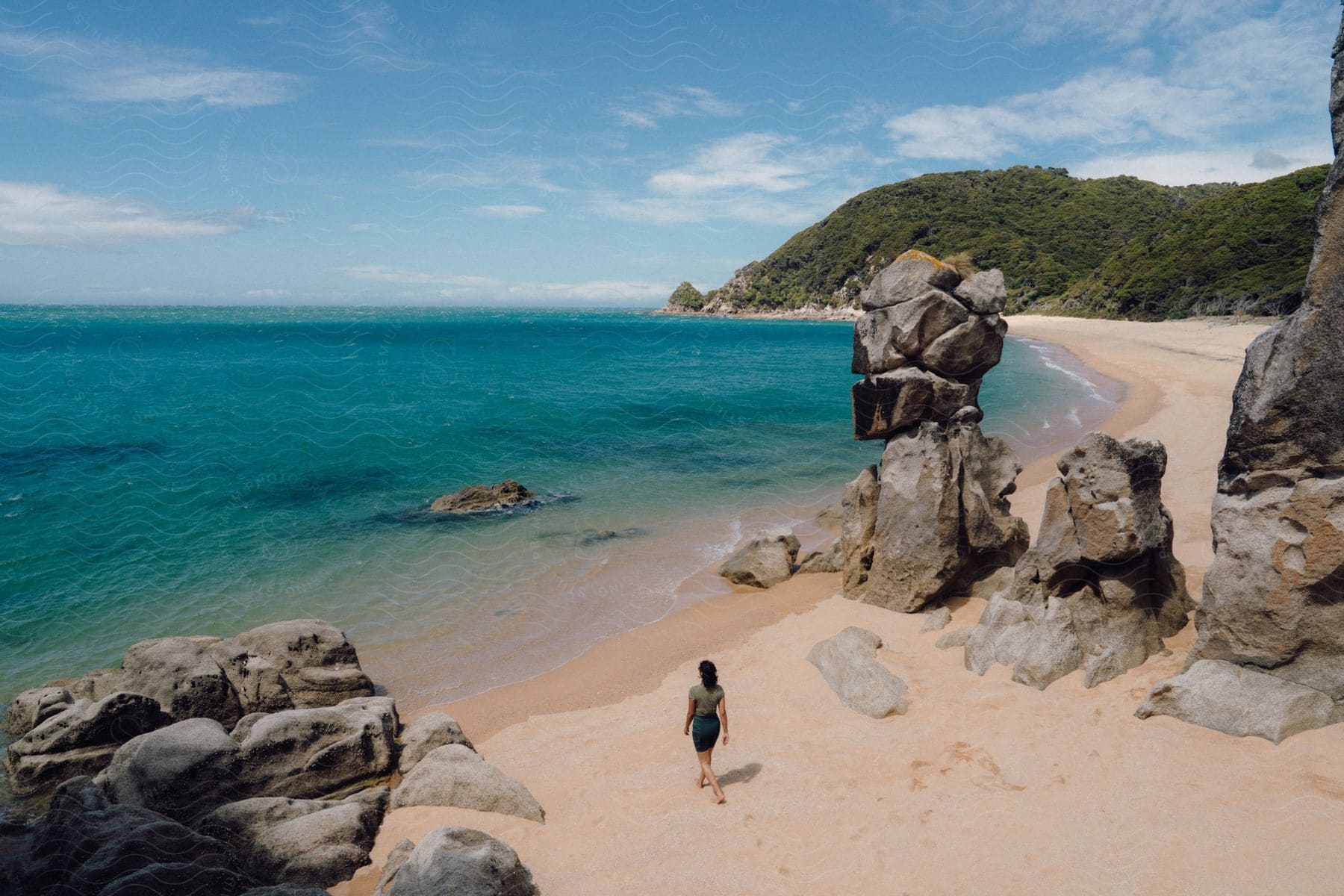 A young woman walks alone on a tropical beach next to rock formations and the sea