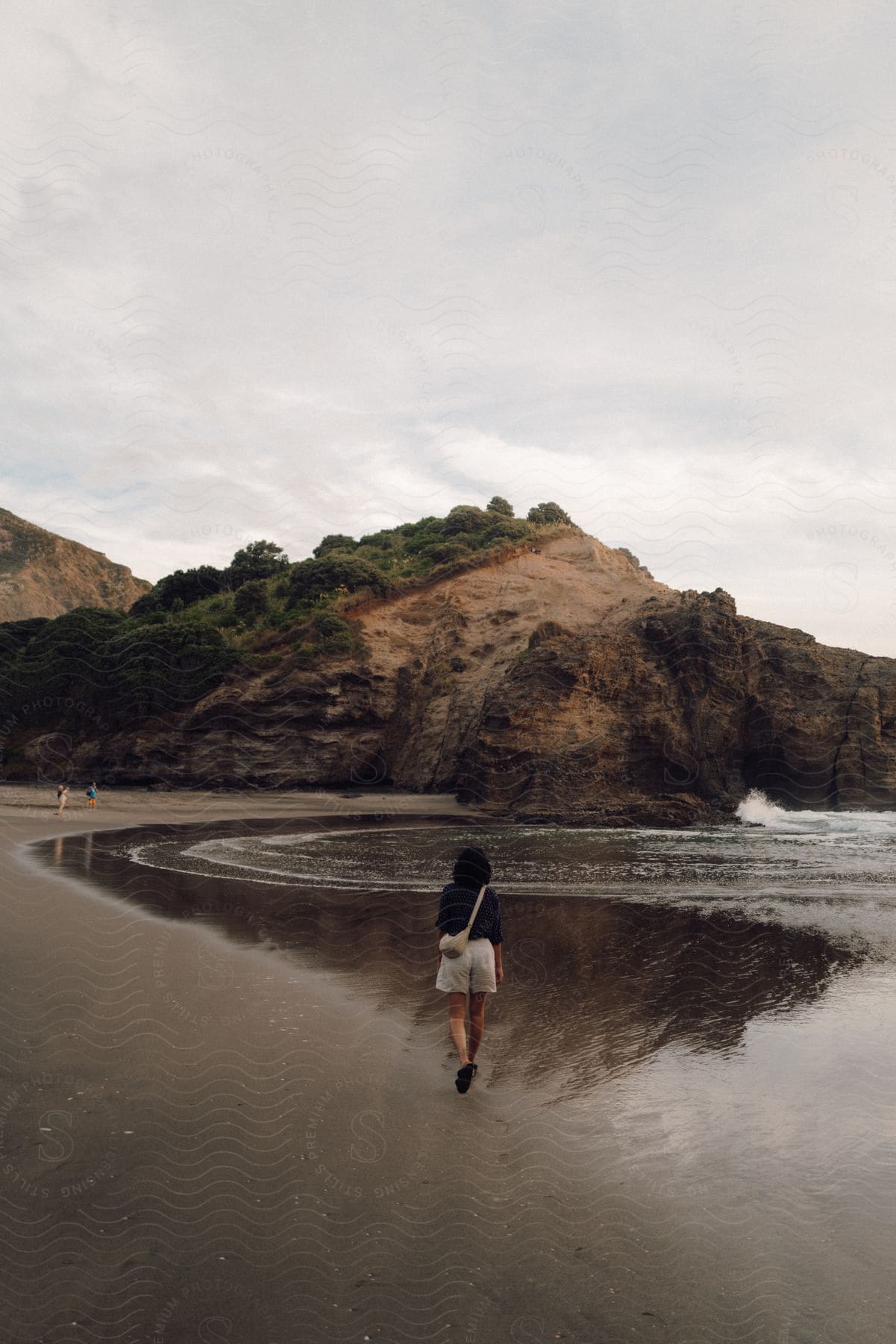 A woman wearing a dark blue shirt and beige shorts walks along the beach near the sea on a cloudy day.