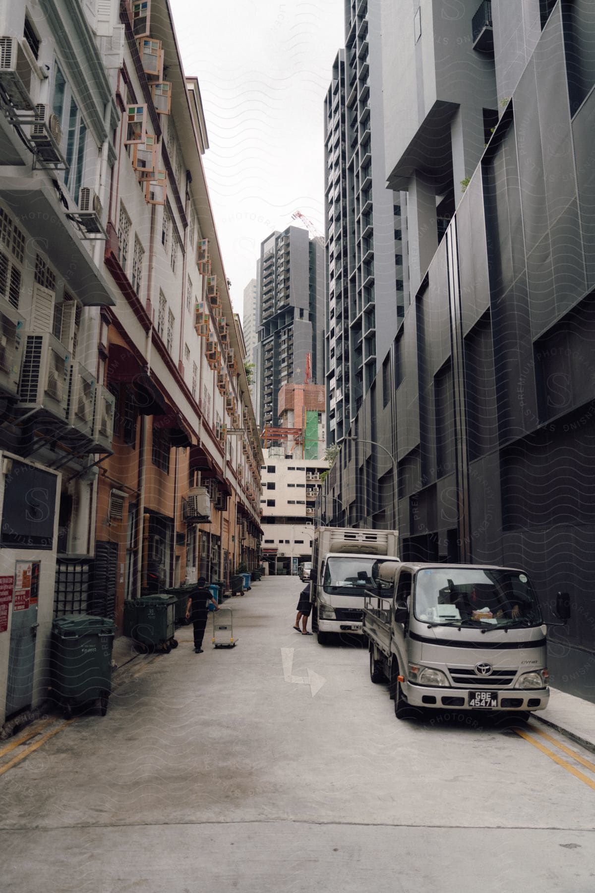 People near trucks parked in a downtown alley with a skyscraper in the distance