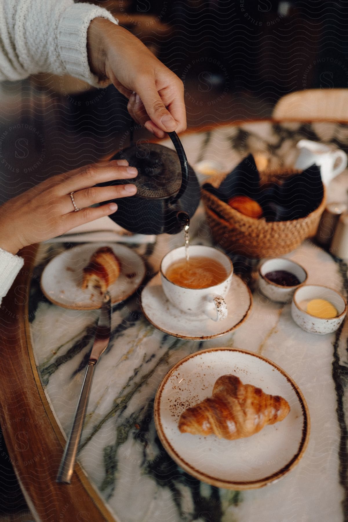 Woman pours tea onto table with plated croissants.