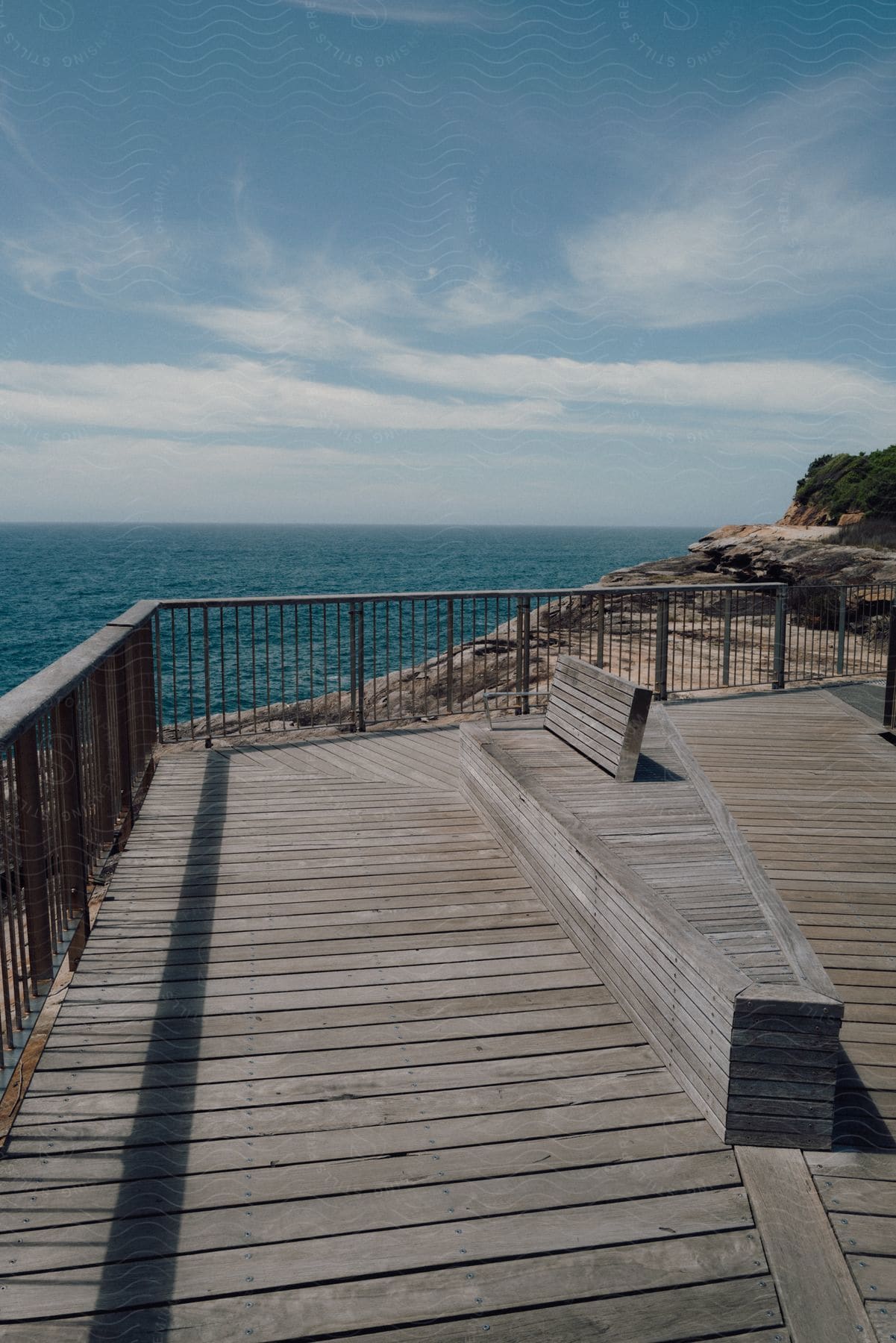 Wooden deck on the edge of a rocky coast overlooking an expanse of blue sea on a clear day.